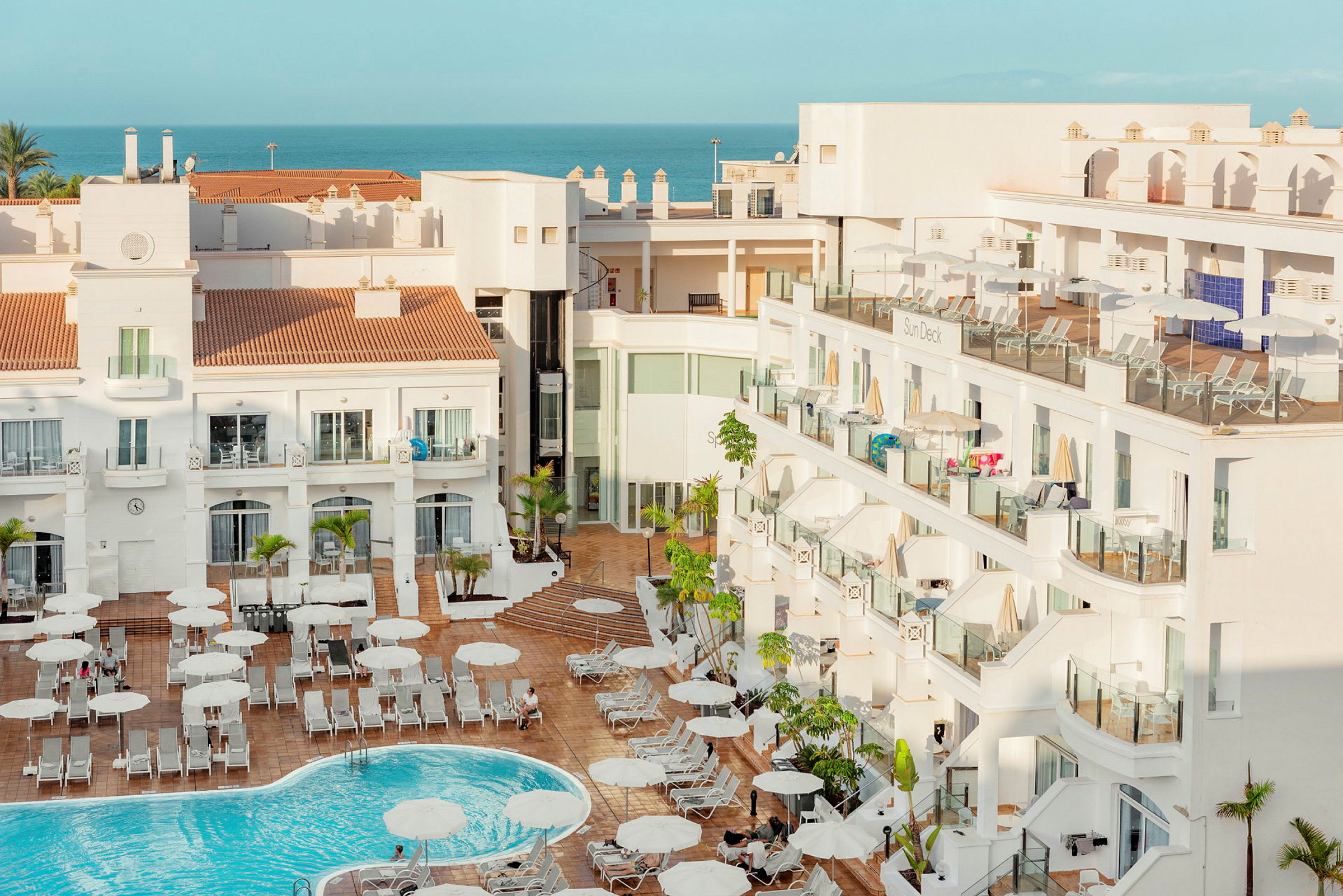 Hotellbyggnad med pool och solstolar utomhus. (AI-genererad text)