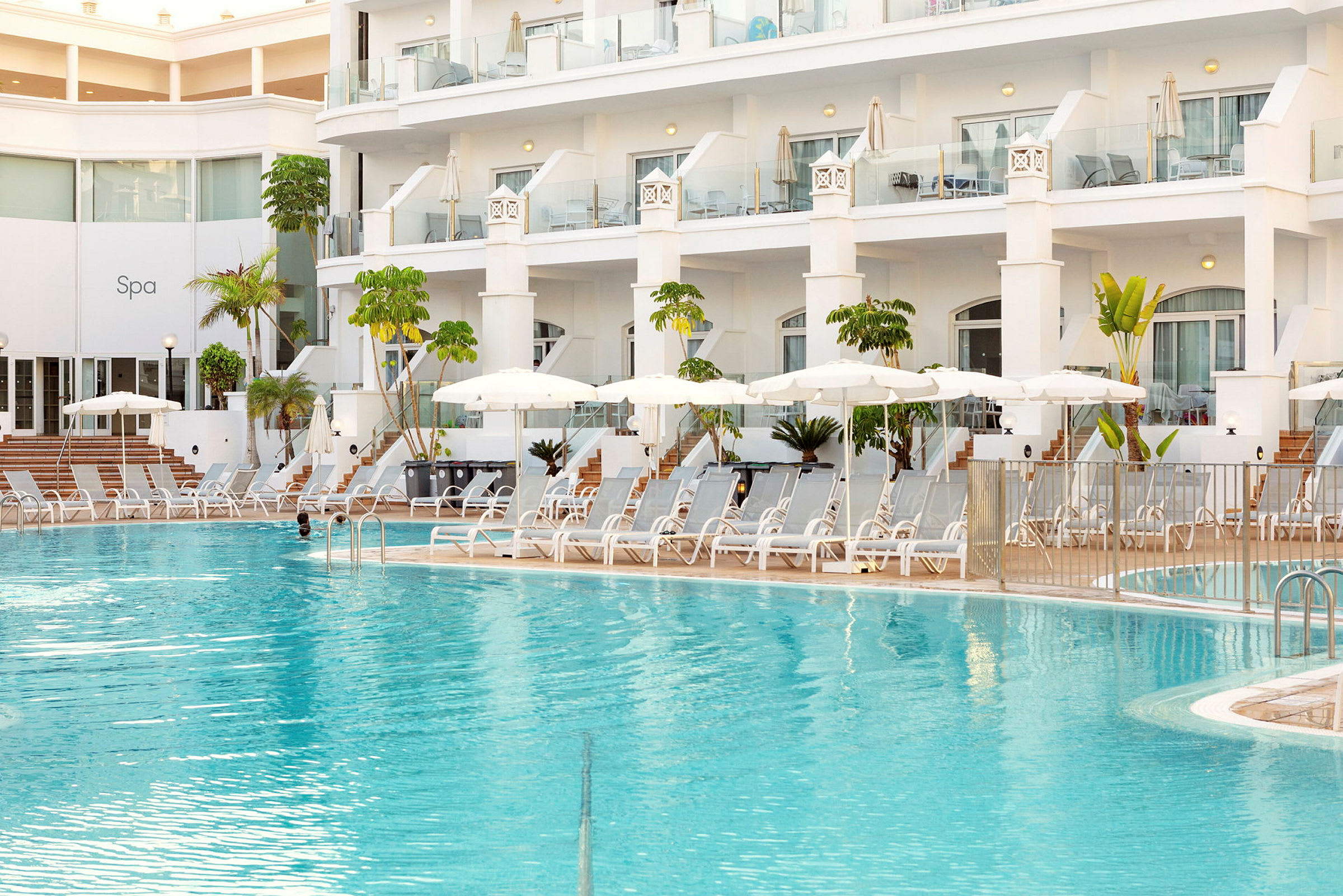 Hotellpool med solstolar och parasoller vid en modern byggnad. (AI-genererad text)