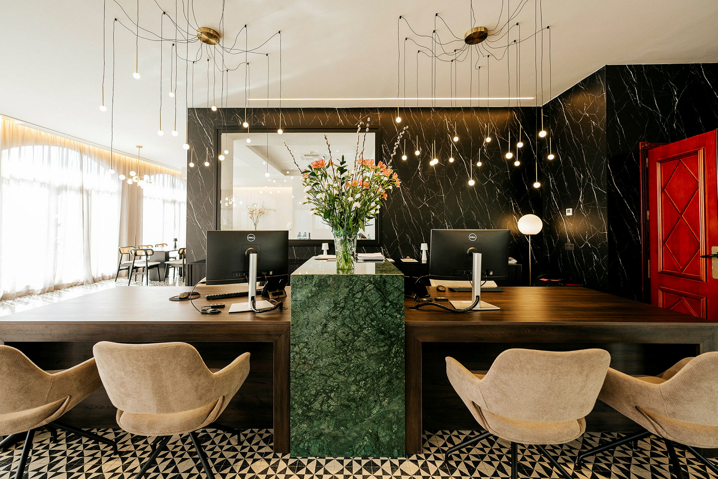 Reception med två skrivbord, kontorsstolar och en grön marmorpelare med blommor. (AI-genererad text)