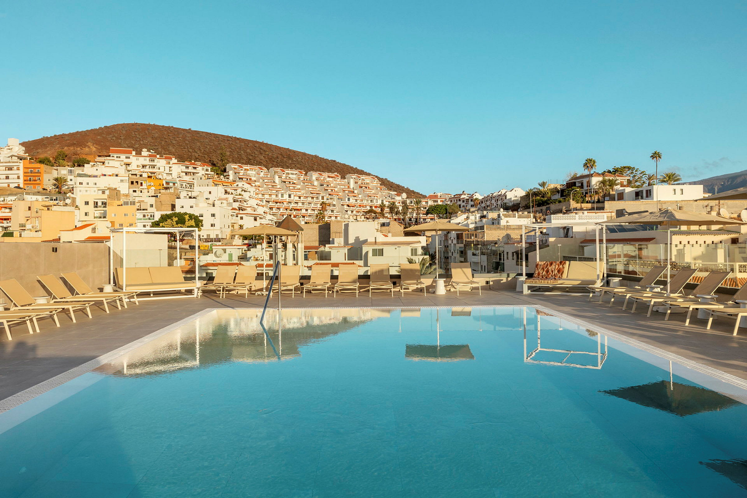 En swimmingpool med solstolar på en terrass och hus i bakgrunden. (AI-genererad text)
