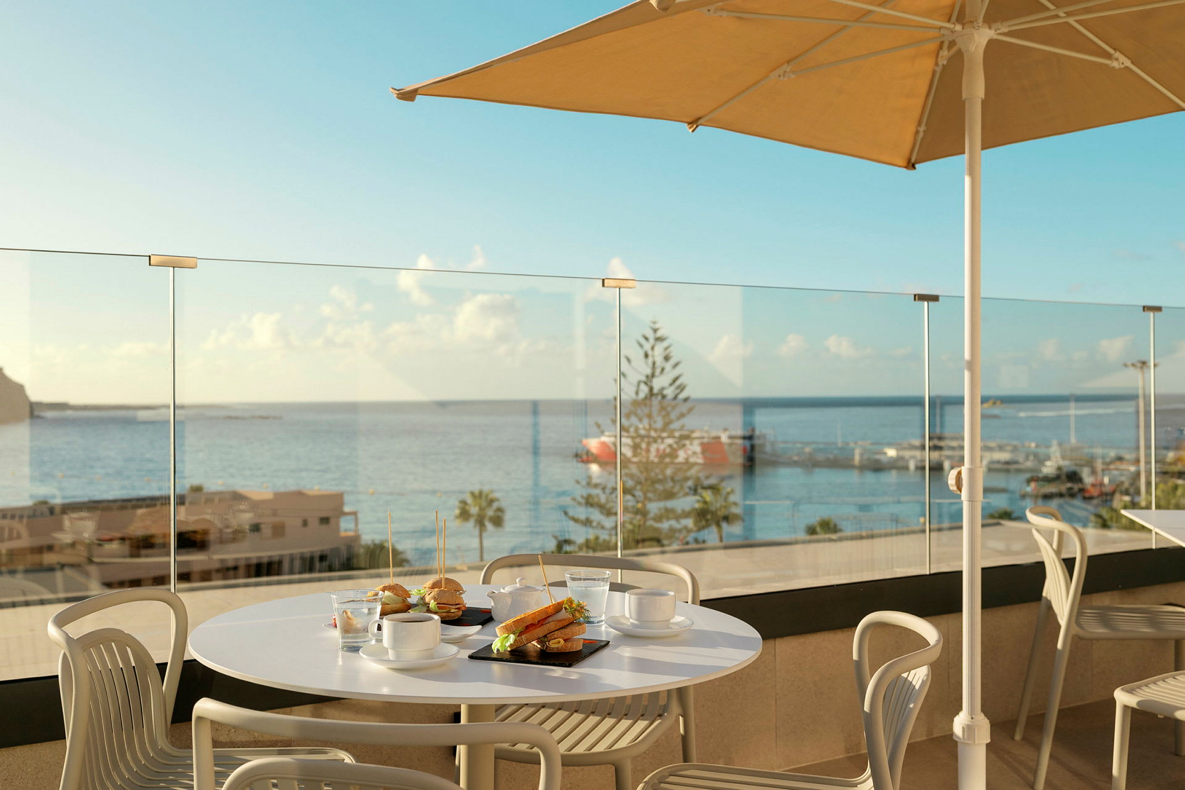 En matplats med bord och stolar på en terrass med utsikt över havet. (AI-genererad text)