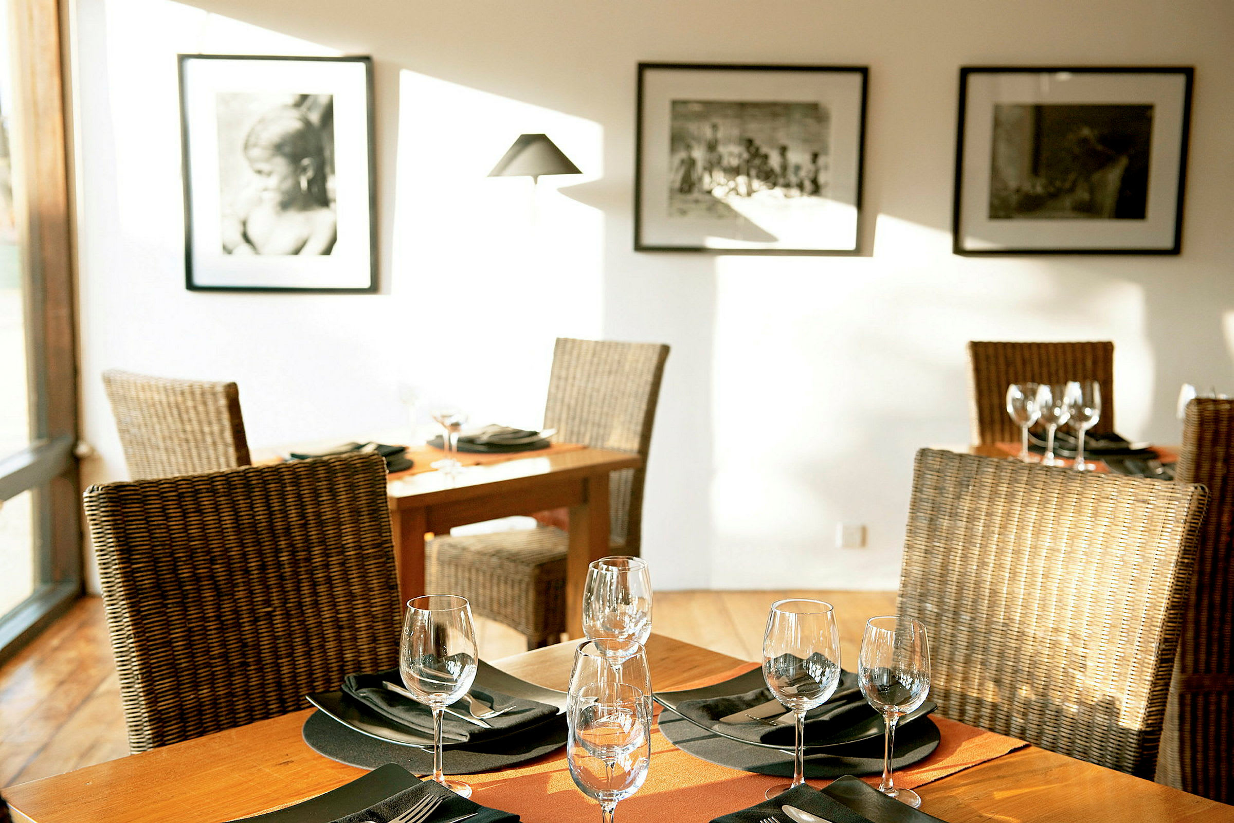 Ett elegant restaurangbord med dukning, omgiven av rottingstolar och dekorerat med glas och servetter. Väggarna dekorerade med svartvita fotografier. (AI-genererad text)