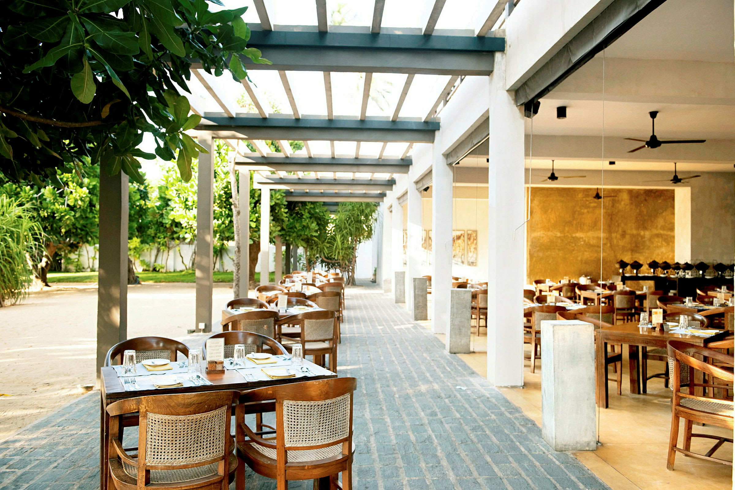 Utomhusrestaurang med bord och stolar arrangerade under en pergola. (AI-genererad text)