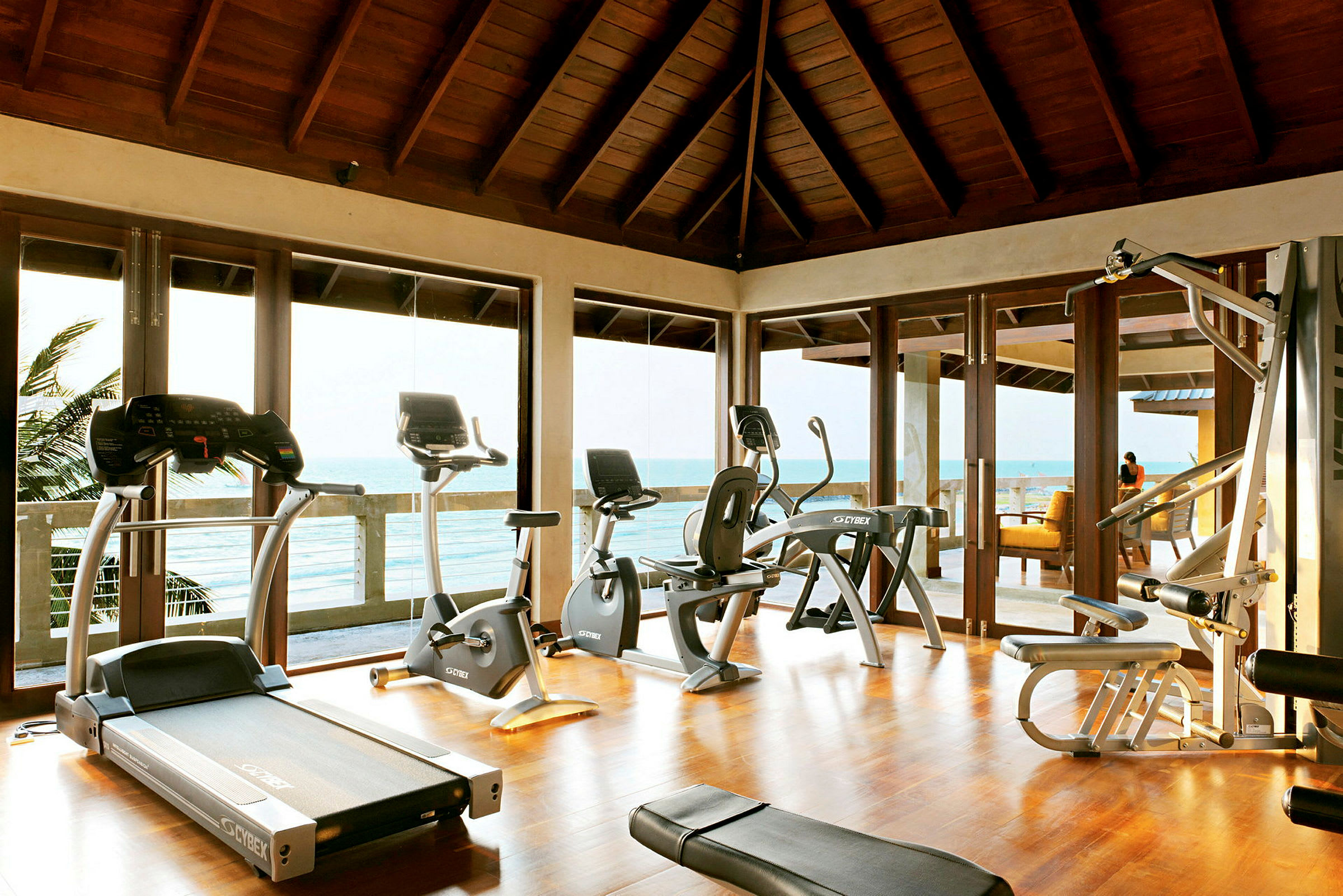 Ett gym med träningsmaskiner framför stora fönster med utsikt över havet. (AI-genererad text)
