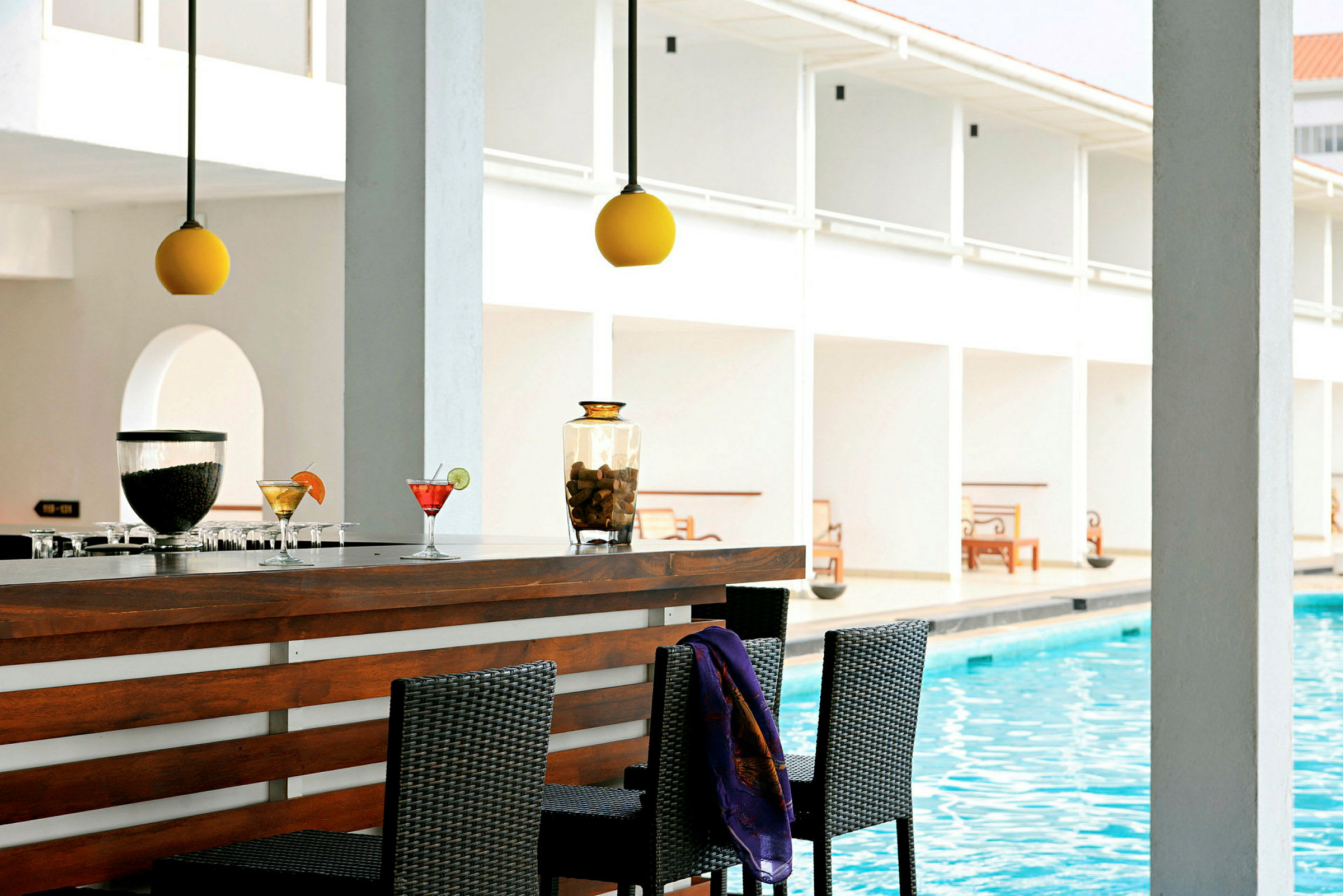 En bar vid en pool med några drinkar samt belysning ovanför och sittplatser framför. (AI-genererad text)