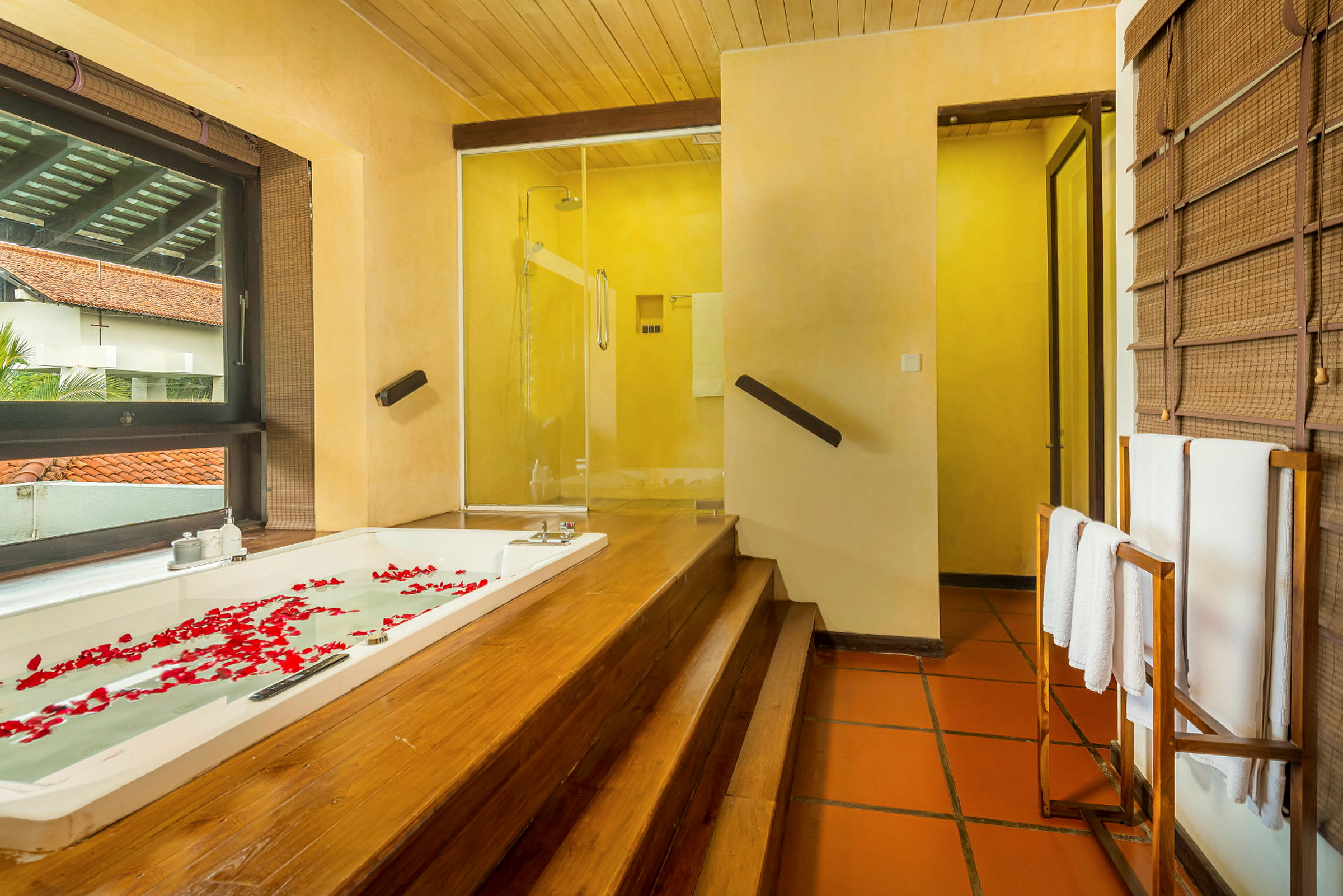 Ett badrum med träpaneler, en jacuzzi fylld med vatten och rosenblad, samt en dusch i bakgrunden. (AI-genererad text)