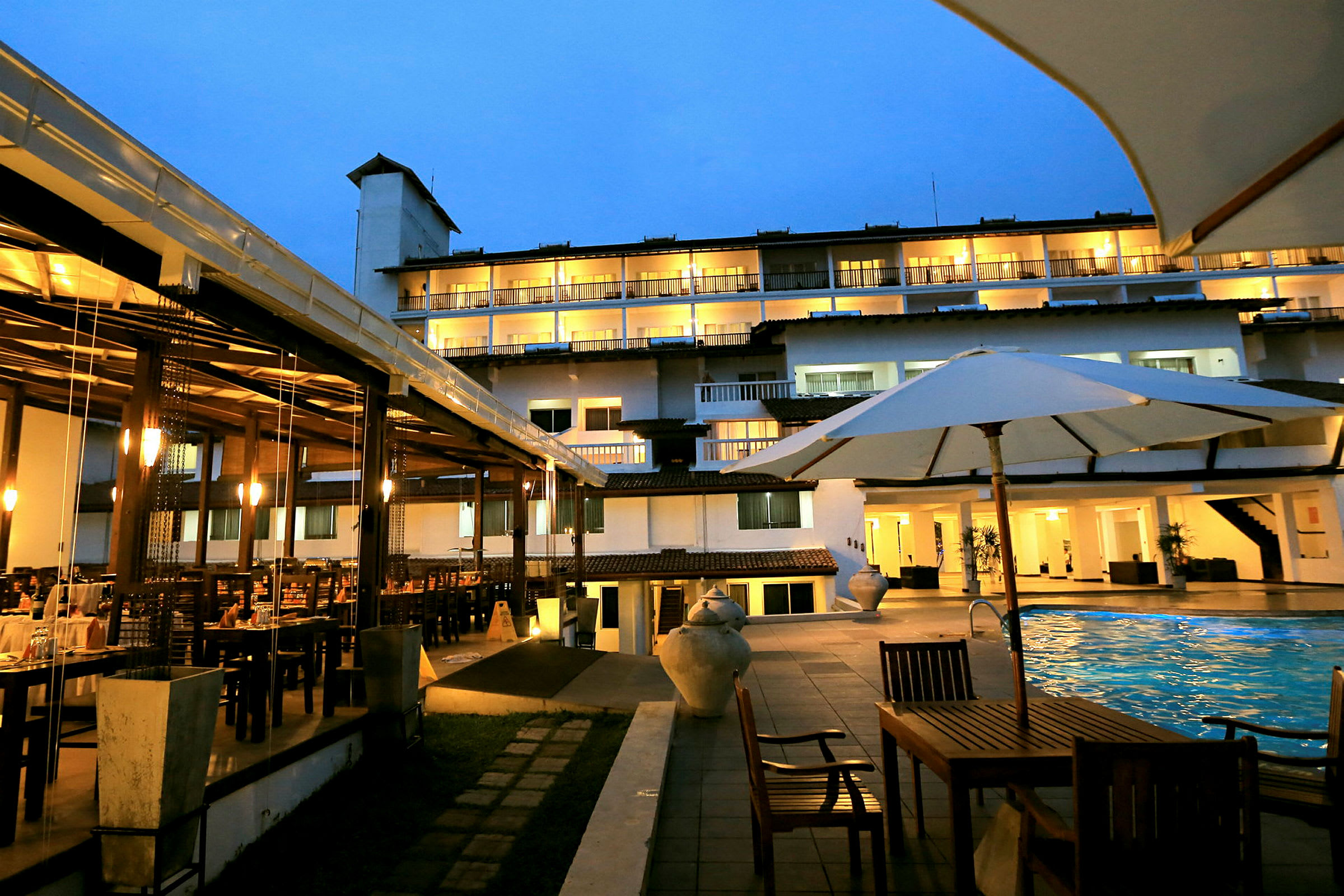 Bild av en hotellbyggnad på kvällen med upplysta balkonger, utomhuspool, trädgårdsmöbler och ett matområde. (AI-genererad text)