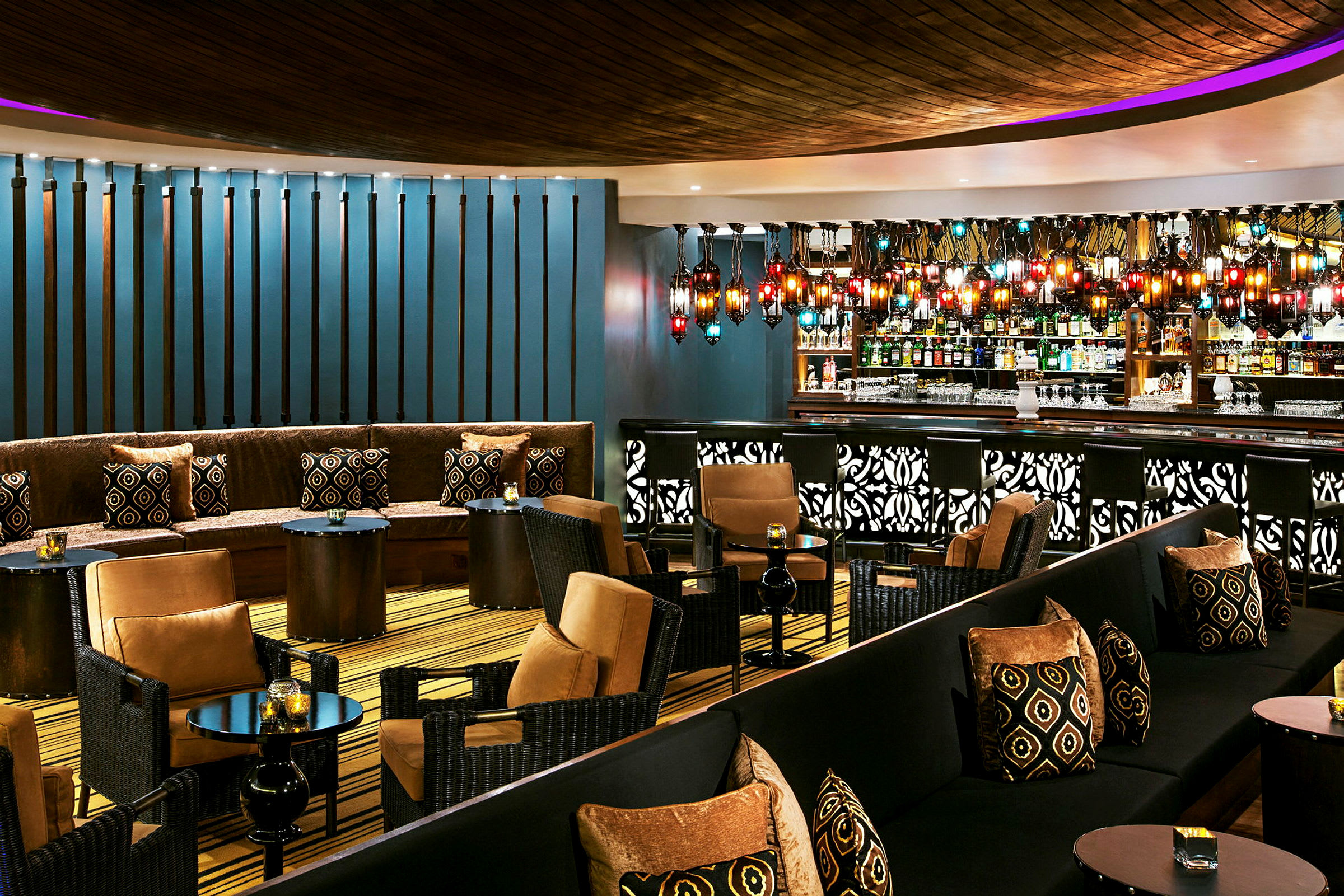 En stilfull lounge med sittplatser, små bord och en bartender. Färgglad belysning och detaljer pryder inredningen. (AI-genererad text)