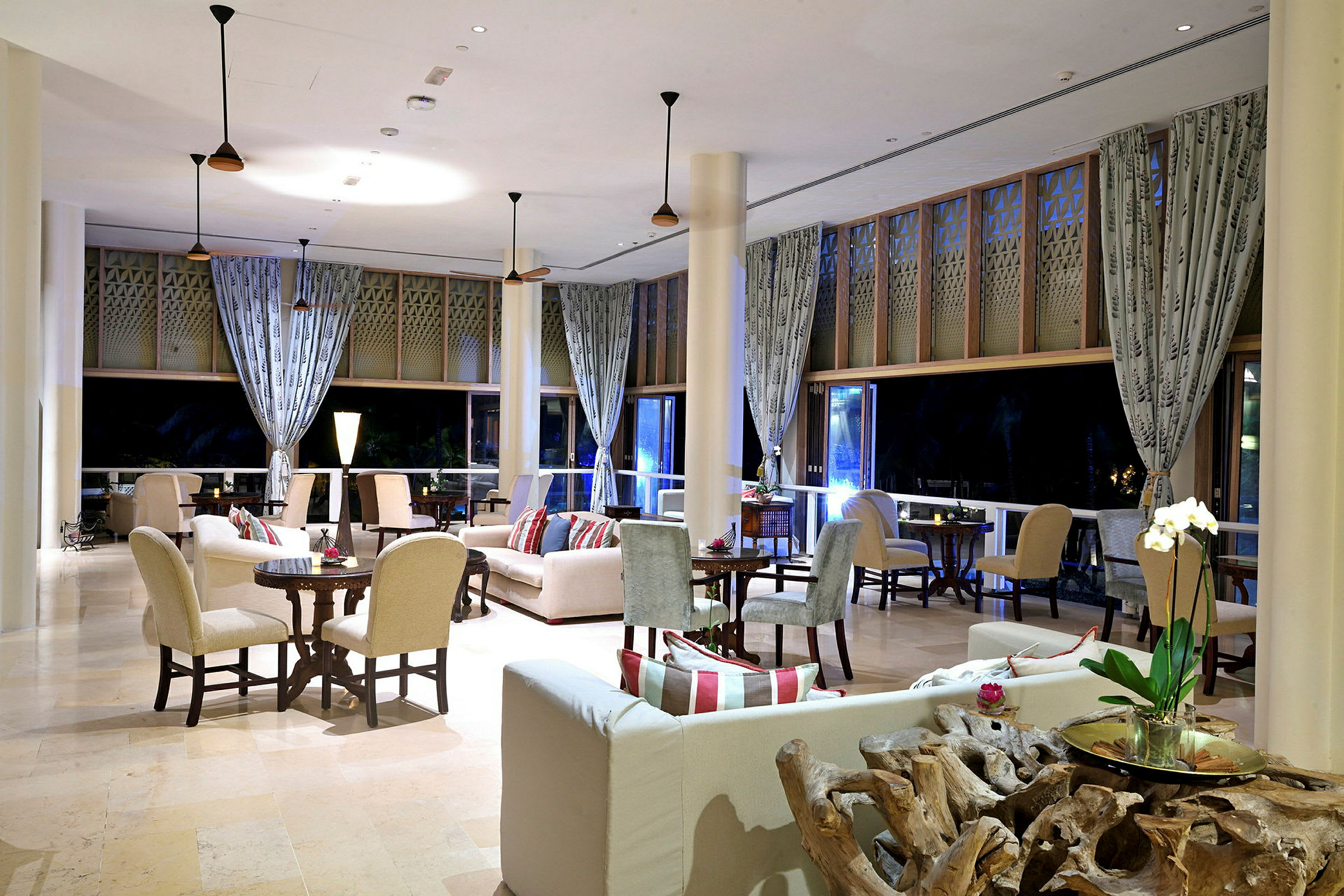 Bild på ett elegant, modernt hotellobbyområde med soffgrupper, stolar och bord, stora fönster och gardiner. (AI-genererad text)