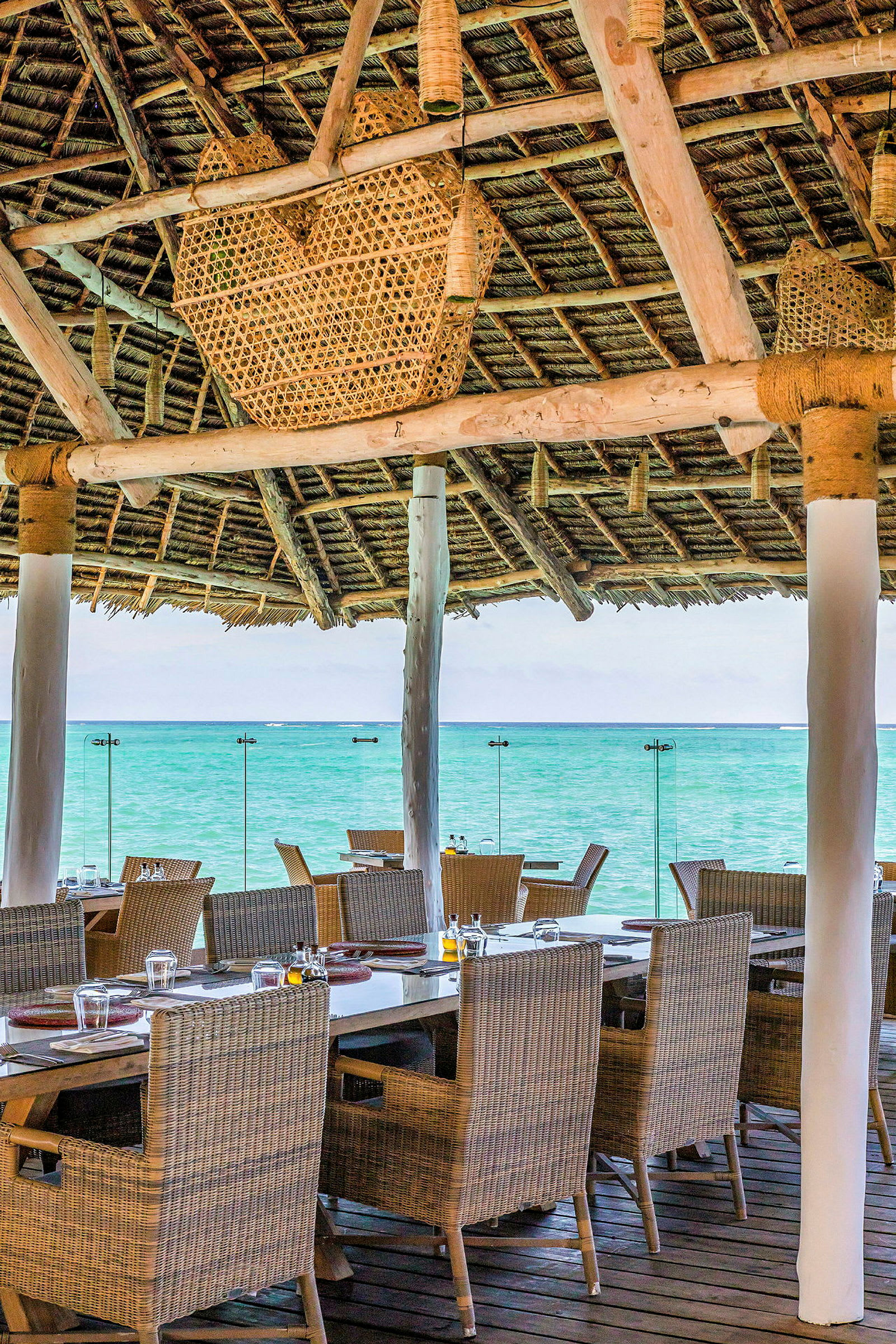 Restaurangens sittplatser vid havet, med bord och stolar under ett tak av trä och halm. (AI-genererad text)