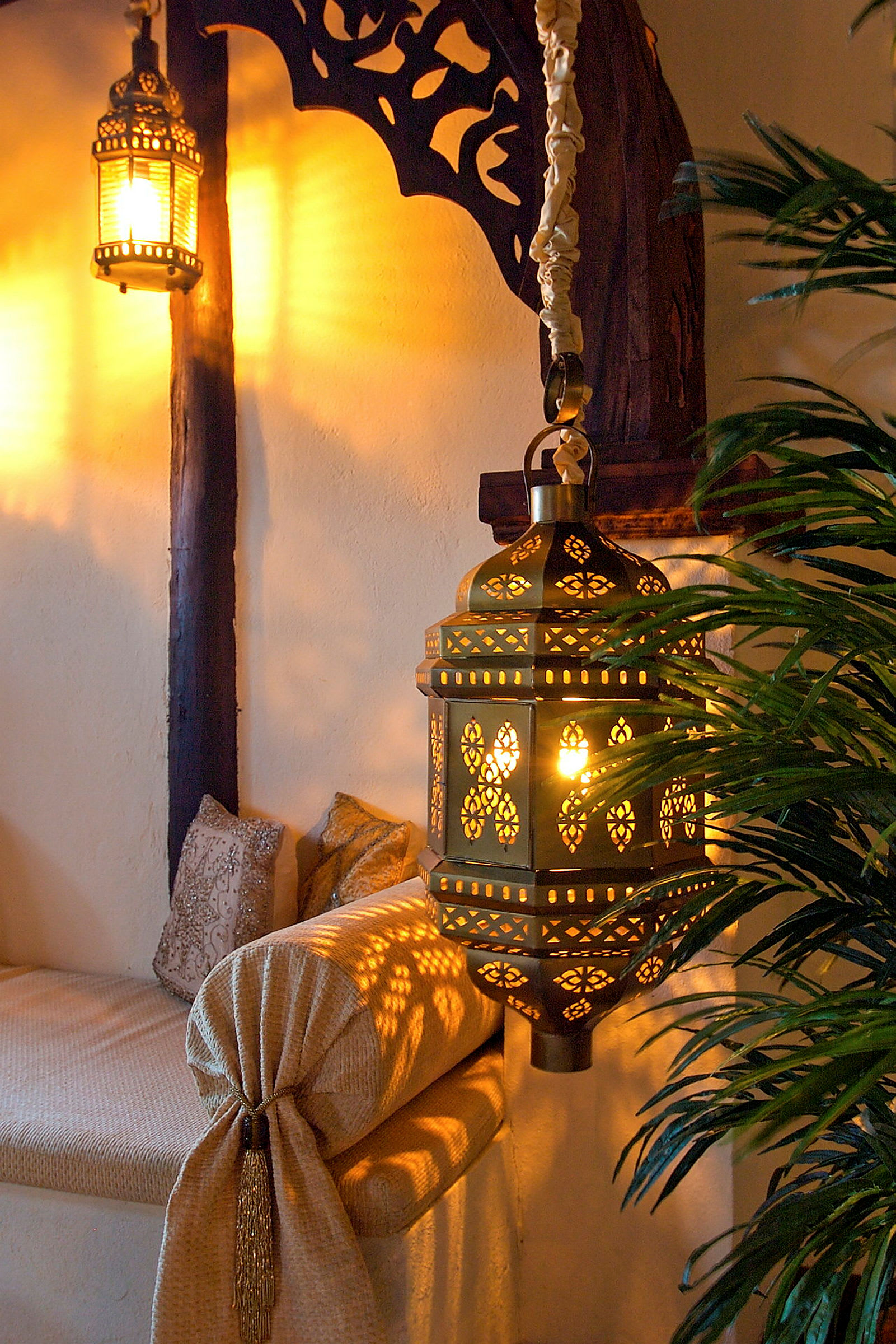 En upplyst orientaliskt inspirerad lampa hänger i interiör med dekorativa detaljer och gardin. (AI-genererad text)
