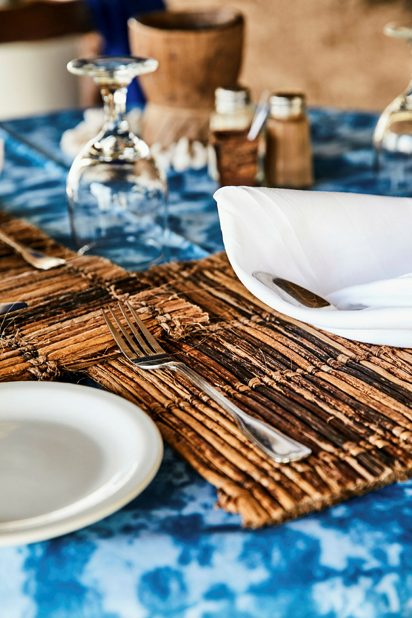 Ett dukat bord med en blå duk, en tallrik, en gaffel, ett glas upp och nedvänd samt kryddor och en servett. (AI-genererad text)