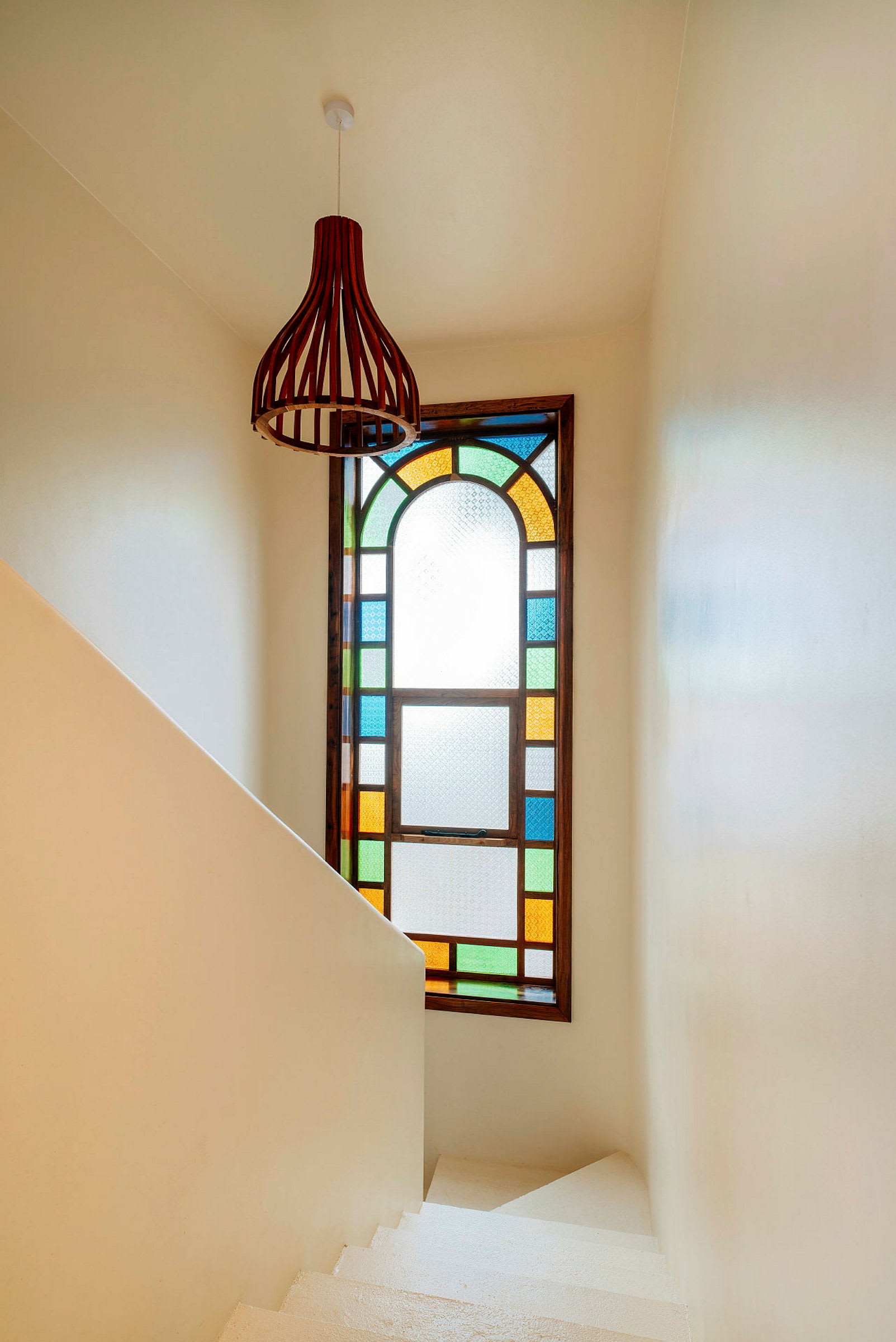 Ett fönster med färgat glas och en modern ljusarmatur på väggen i en vit trappa. (AI-genererad text)