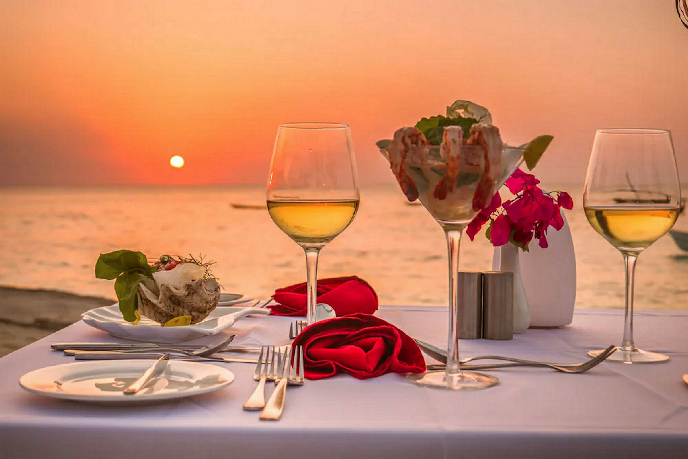 Dukat bord med vin och skaldjur med solnedgång över havet i bakgrunden. (AI-genererad text)