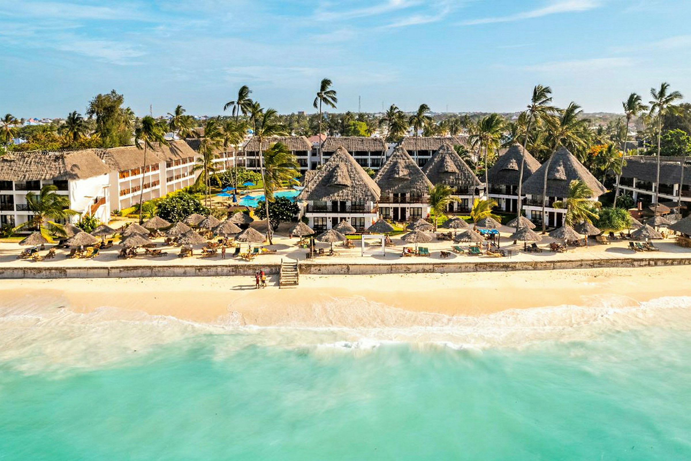 Resort med byggnader och solparasoller vid en sandstrand och klart vatten. (AI-genererad text)