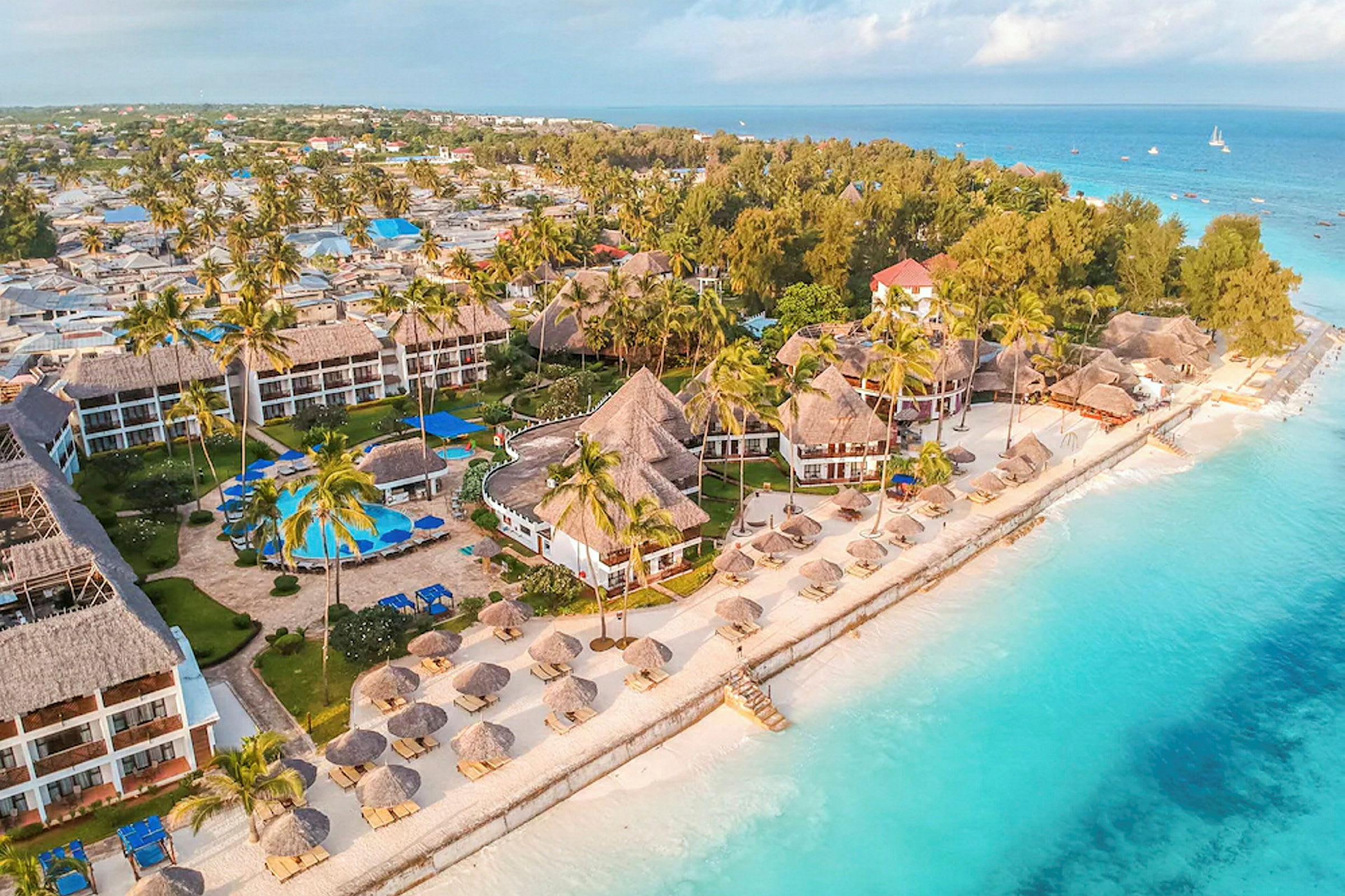 Luftvy som visar en strandnära resort med tropiska byggnader omgivna av palmer nära turkost vatten. (AI-genererad text)