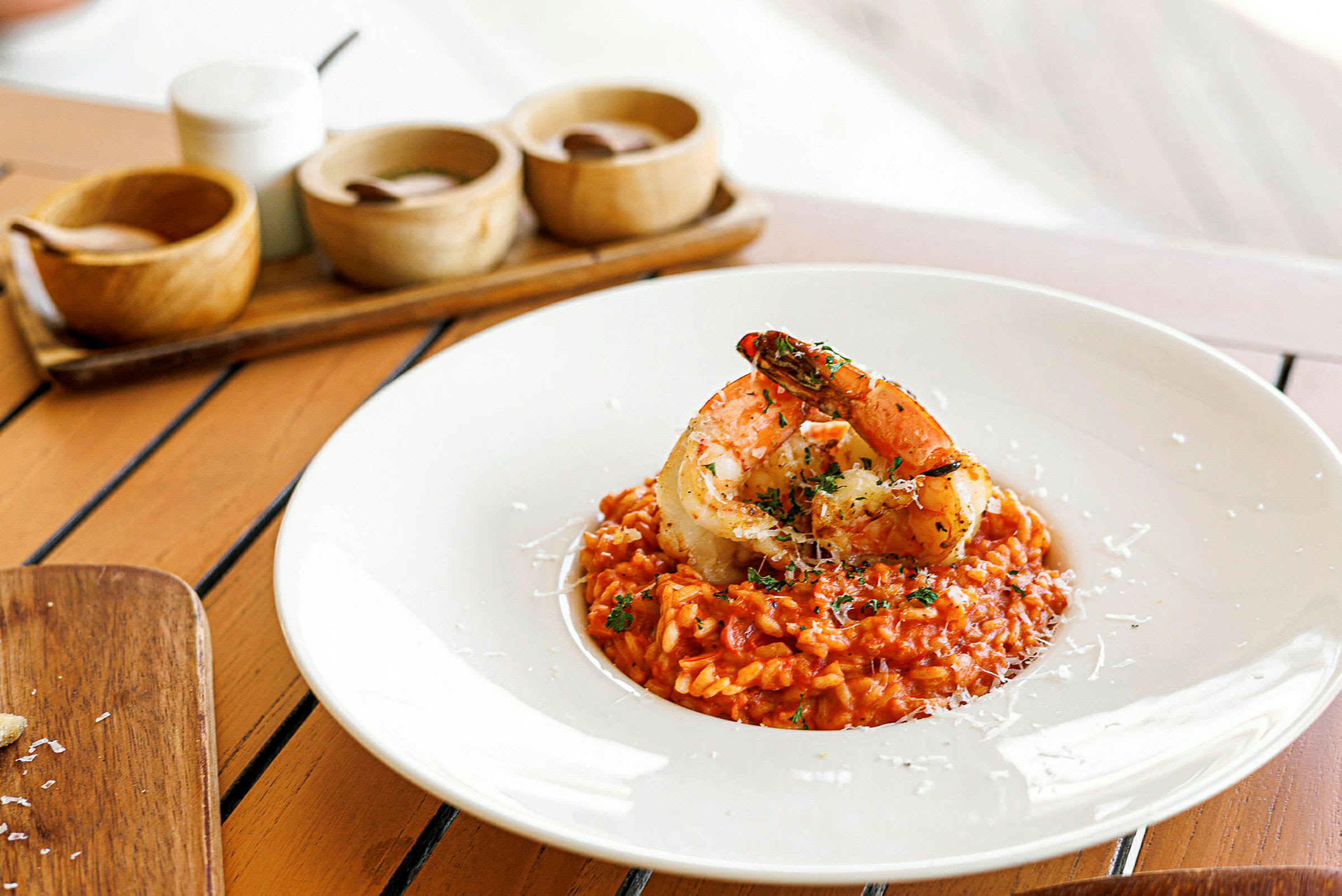 En tallrik med risotto toppad med stora räkor på ett bord. (AI-genererad text)