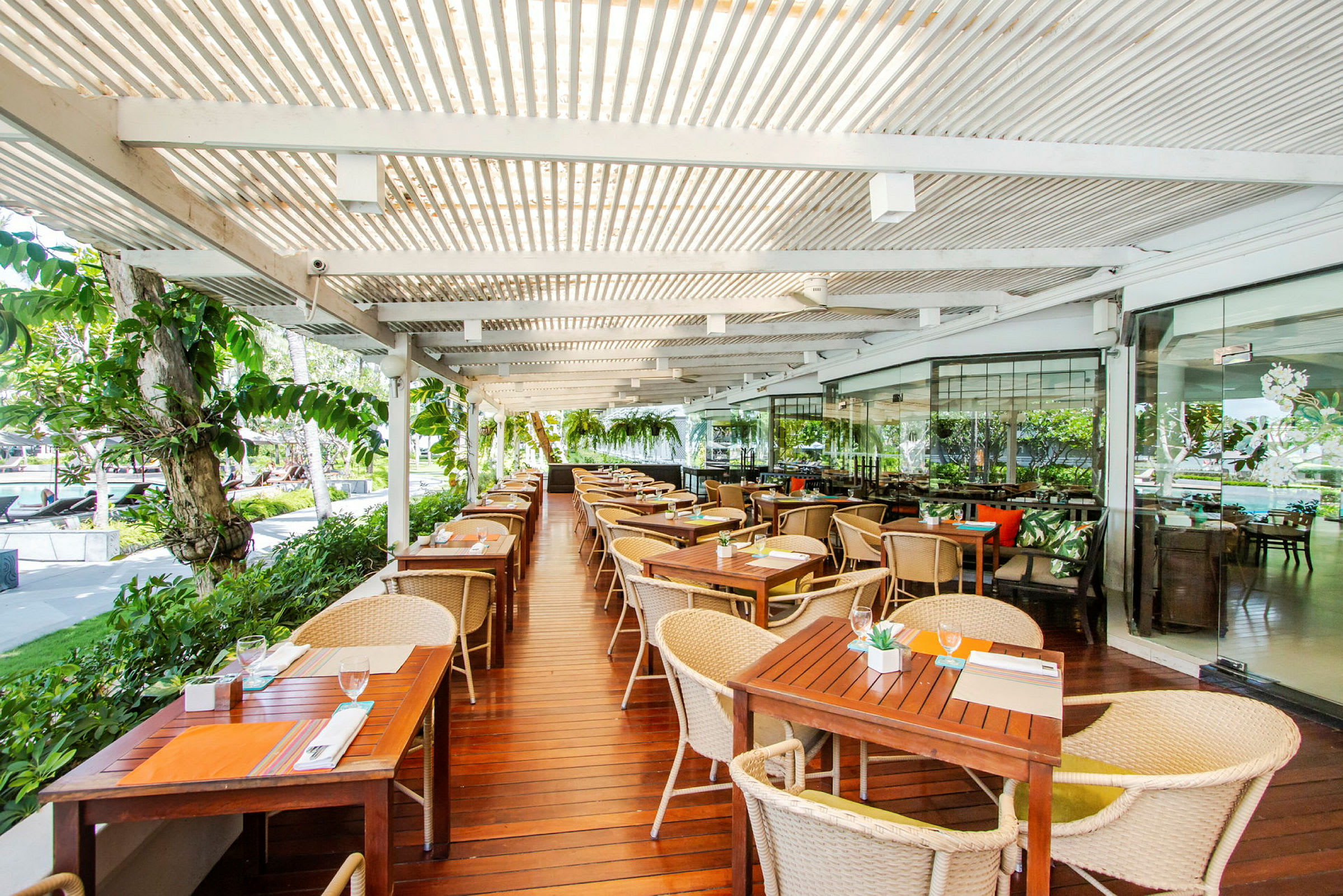 Utomhusrestaurang med träbord och stolar under en överbyggd pergola. (AI-genererad text)