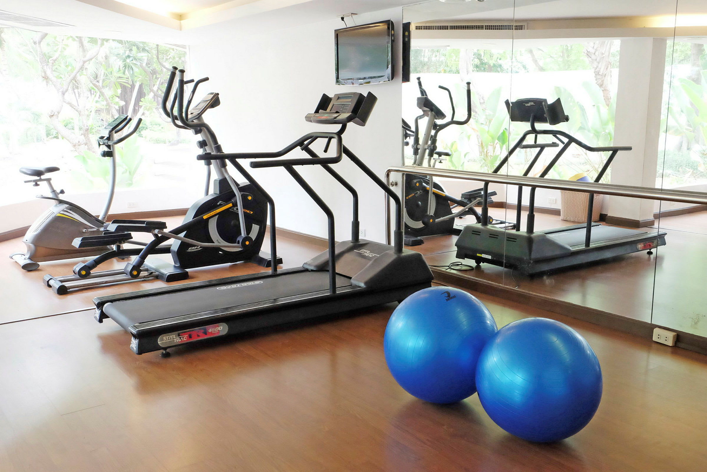 Ett gym med träningsmaskiner, inklusive löpband och motionscykel, samt två blå pilatesbollar. (AI-genererad text)