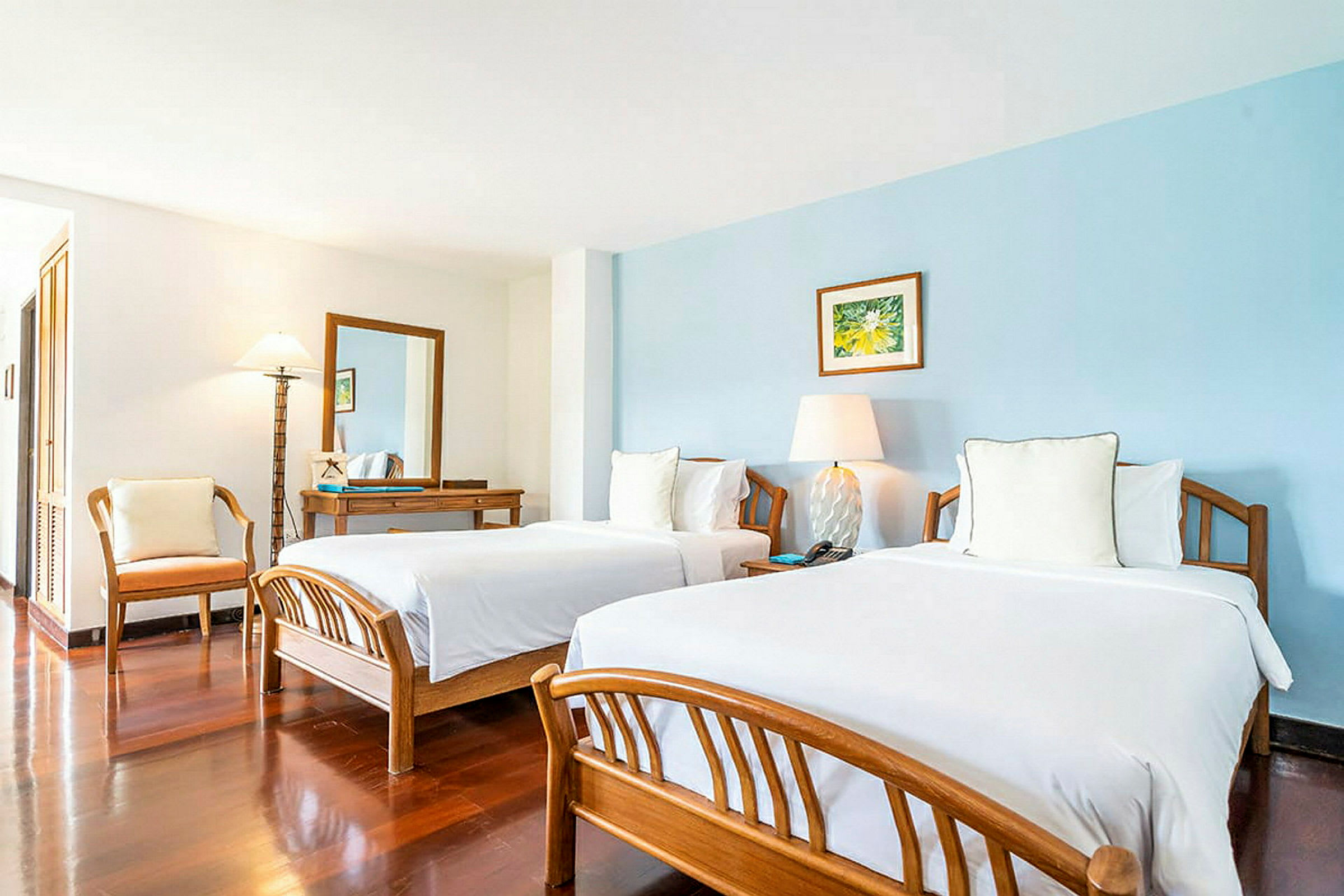 Ett hotellrum med två sängar, ett skrivbord med en spegel och en stol, samt enkla dekorationer. (AI-genererad text)