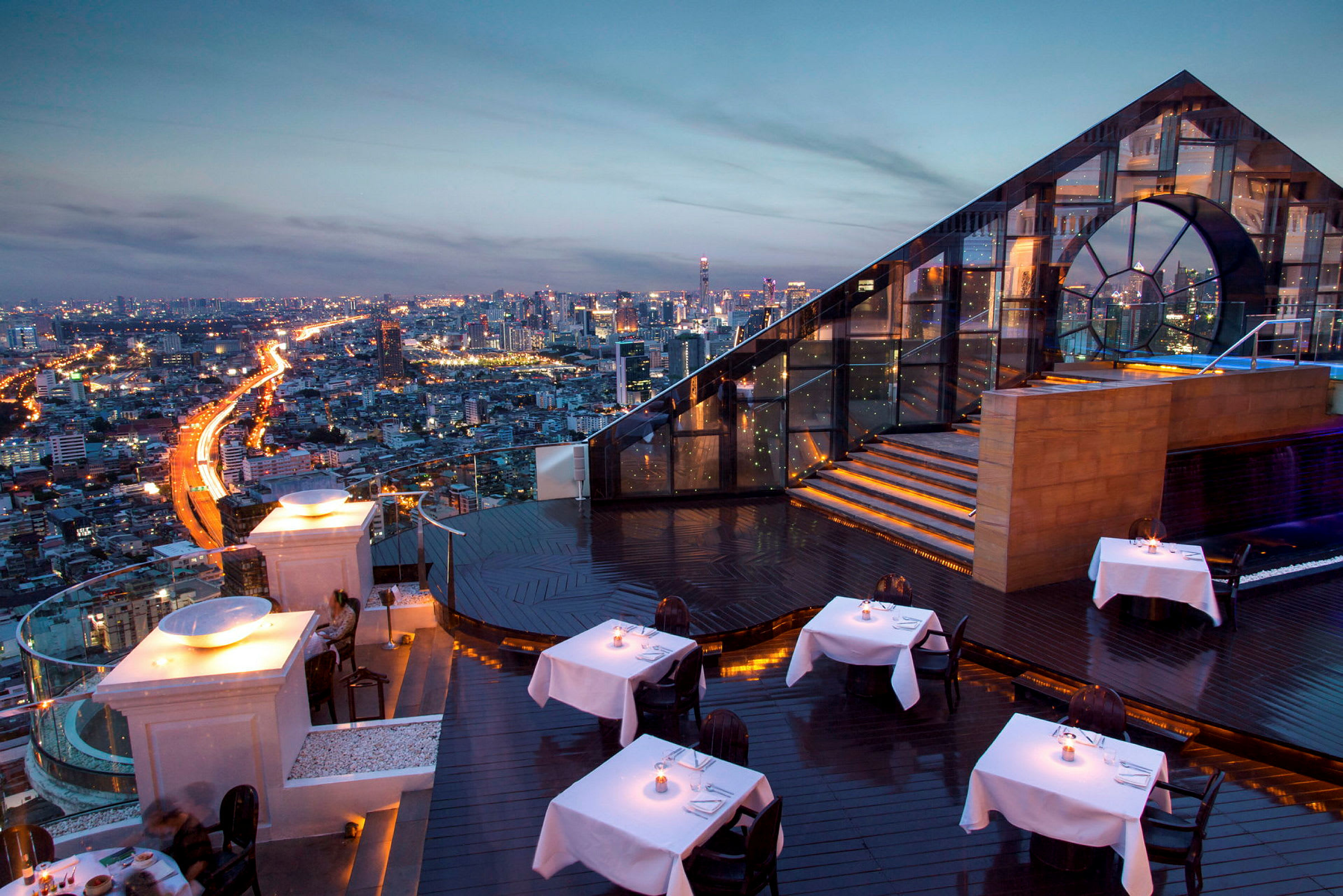 Rooftop-restaurang med belysning och utsikt över en stads skyline i kvällsbelysning. (AI-genererad text)