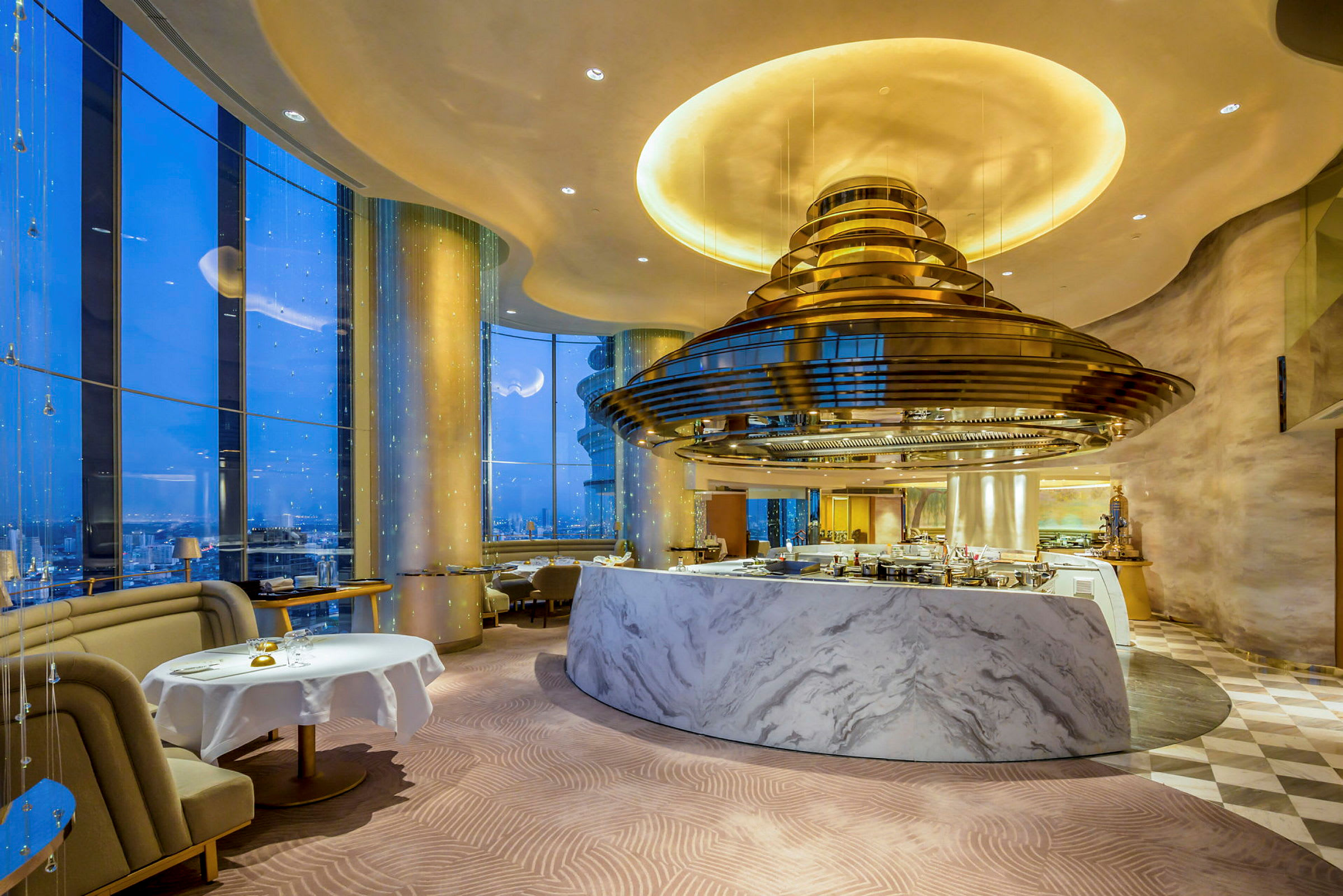En elegant restaurang med marmorinredning och stora fönster som ger utsikt över stadens nattlandskap. (AI-genererad text)