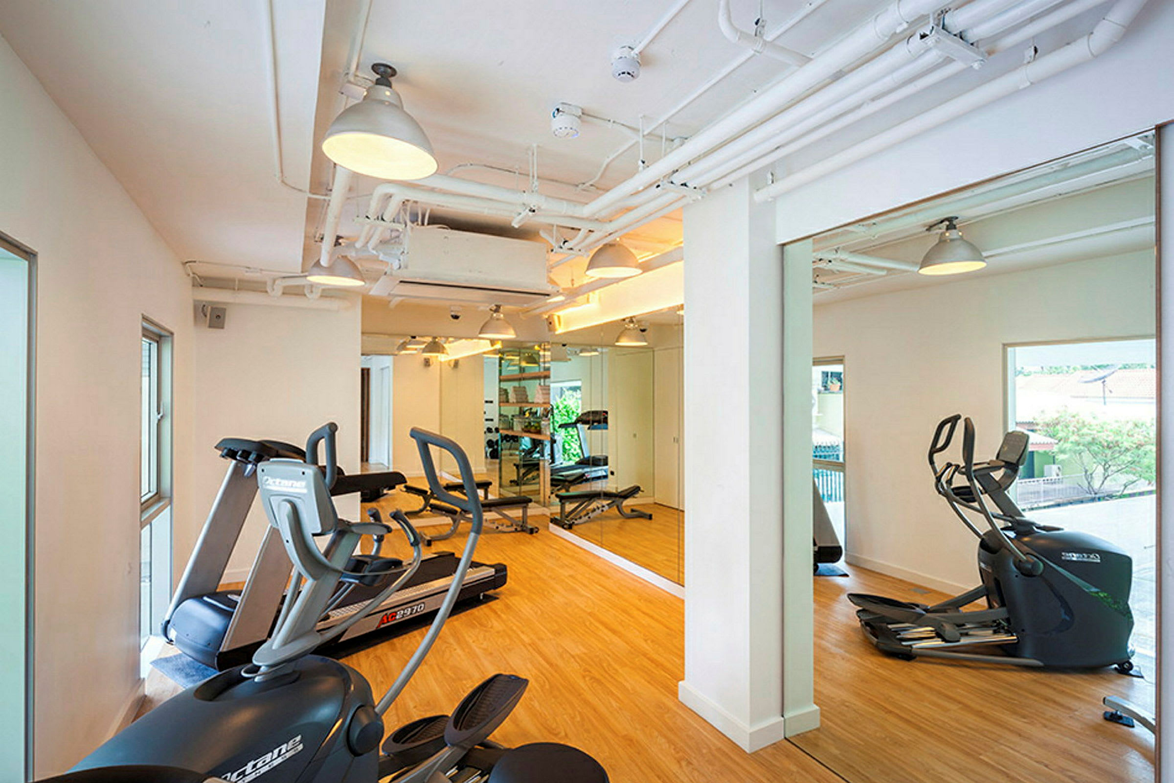 Ett ljust gym med spegelvägg och träningsutrustning som träningscyklar och löpband. (AI-genererad text)
