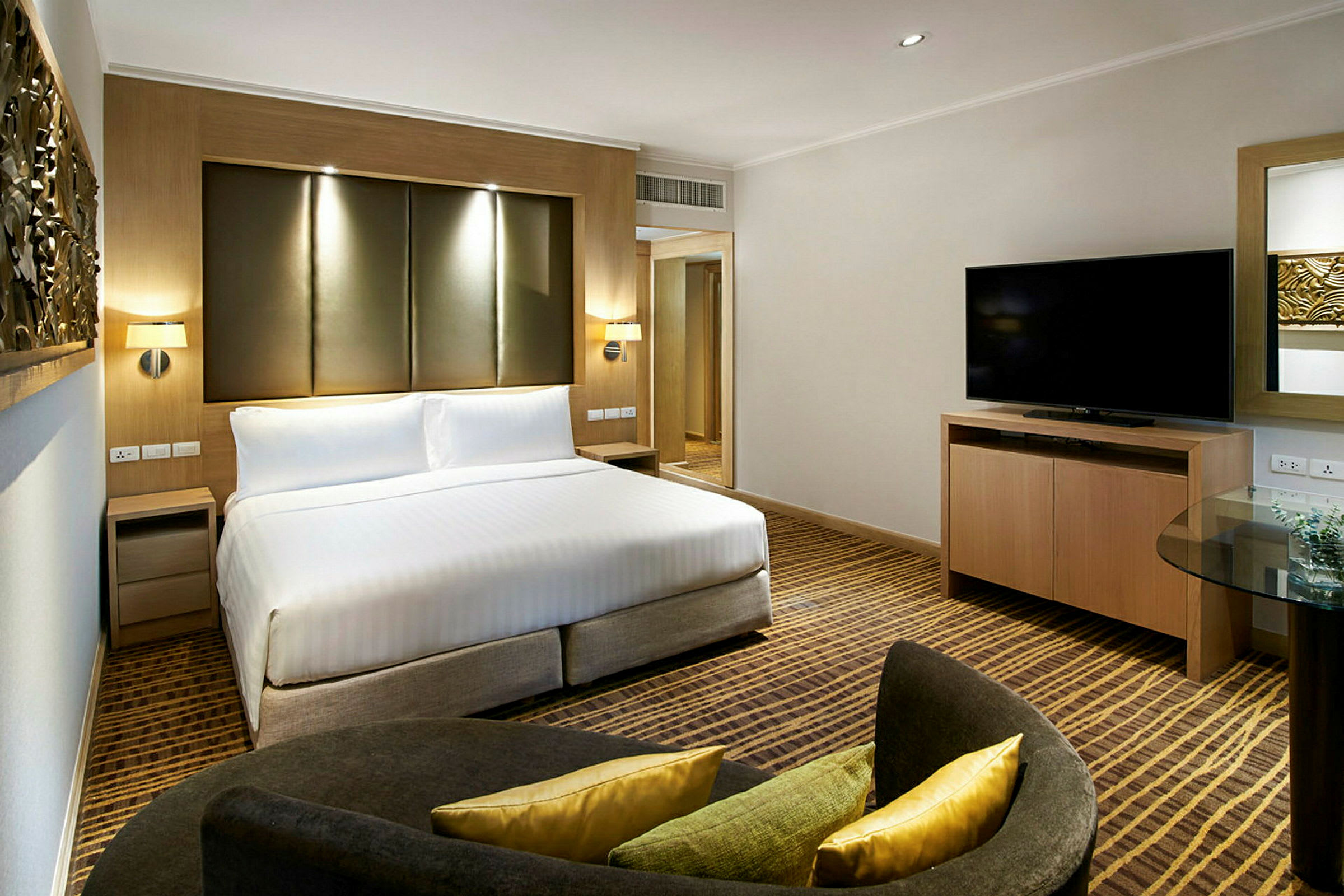 Ett hotellrum med en stor säng, TV på ett träskåp och en sittgrupp med kuddar. (AI-genererad text)
