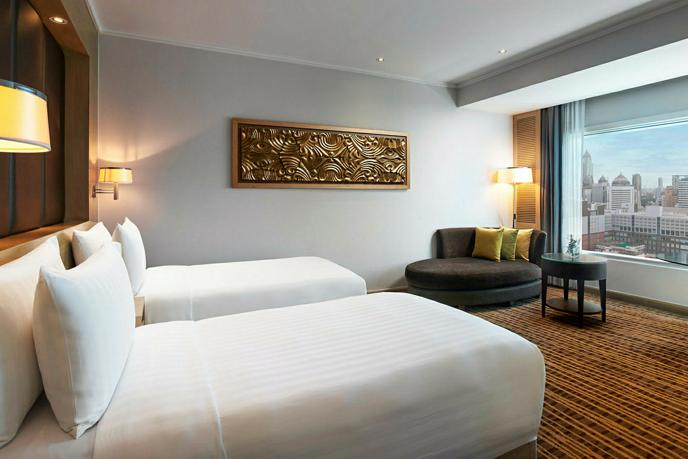 Hotellrum med två enkelsängar, dekoration på väggen och sittplats med utsikt över staden genom ett fönster. (AI-genererad text)