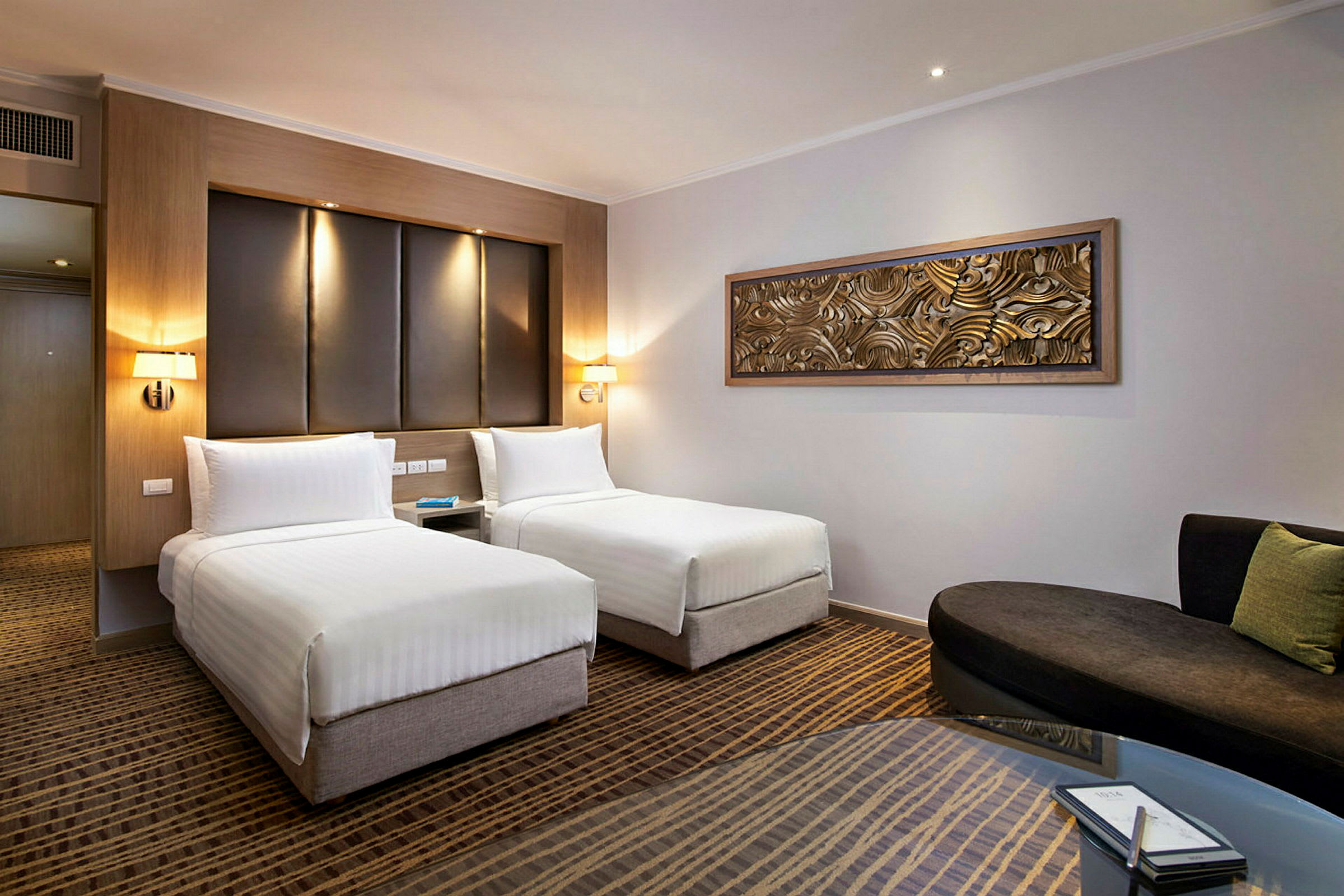 Modernt hotellrum med två enkelsängar, en soffa och ett bord. (AI-genererad text)