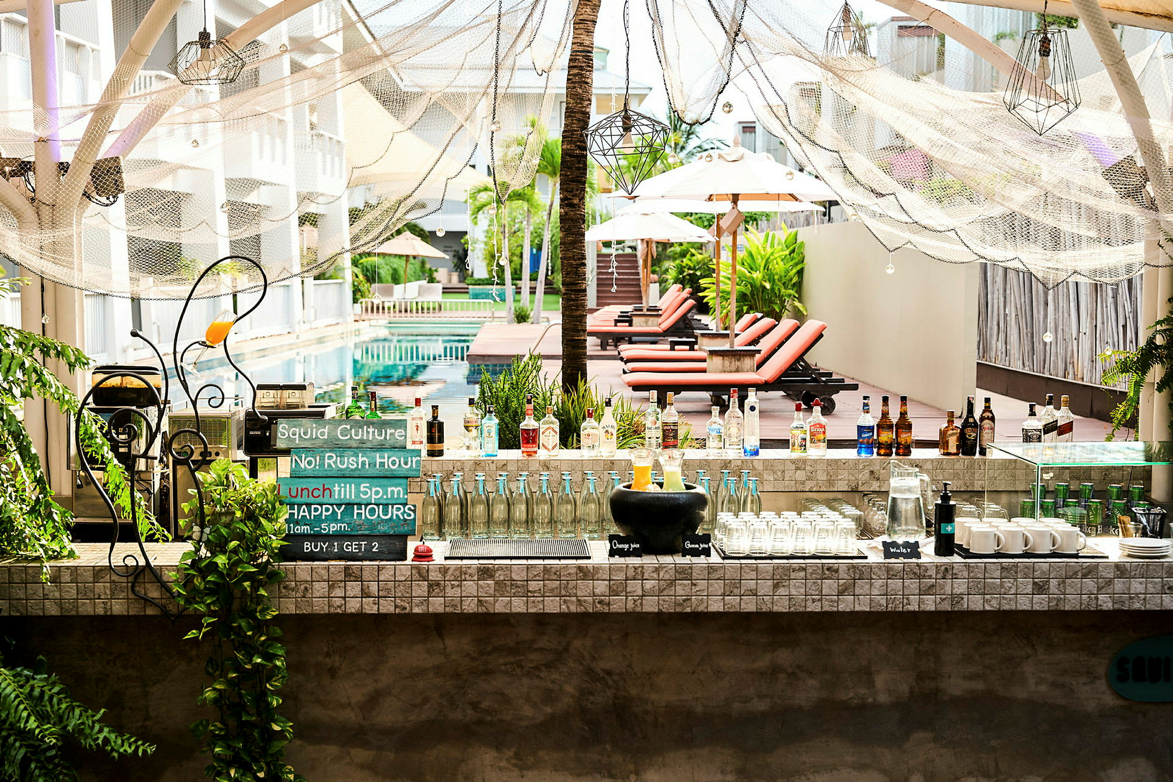 Ett utomhusområde med en pool och vilstolar bakom en bar med drycker. (AI-genererad text)