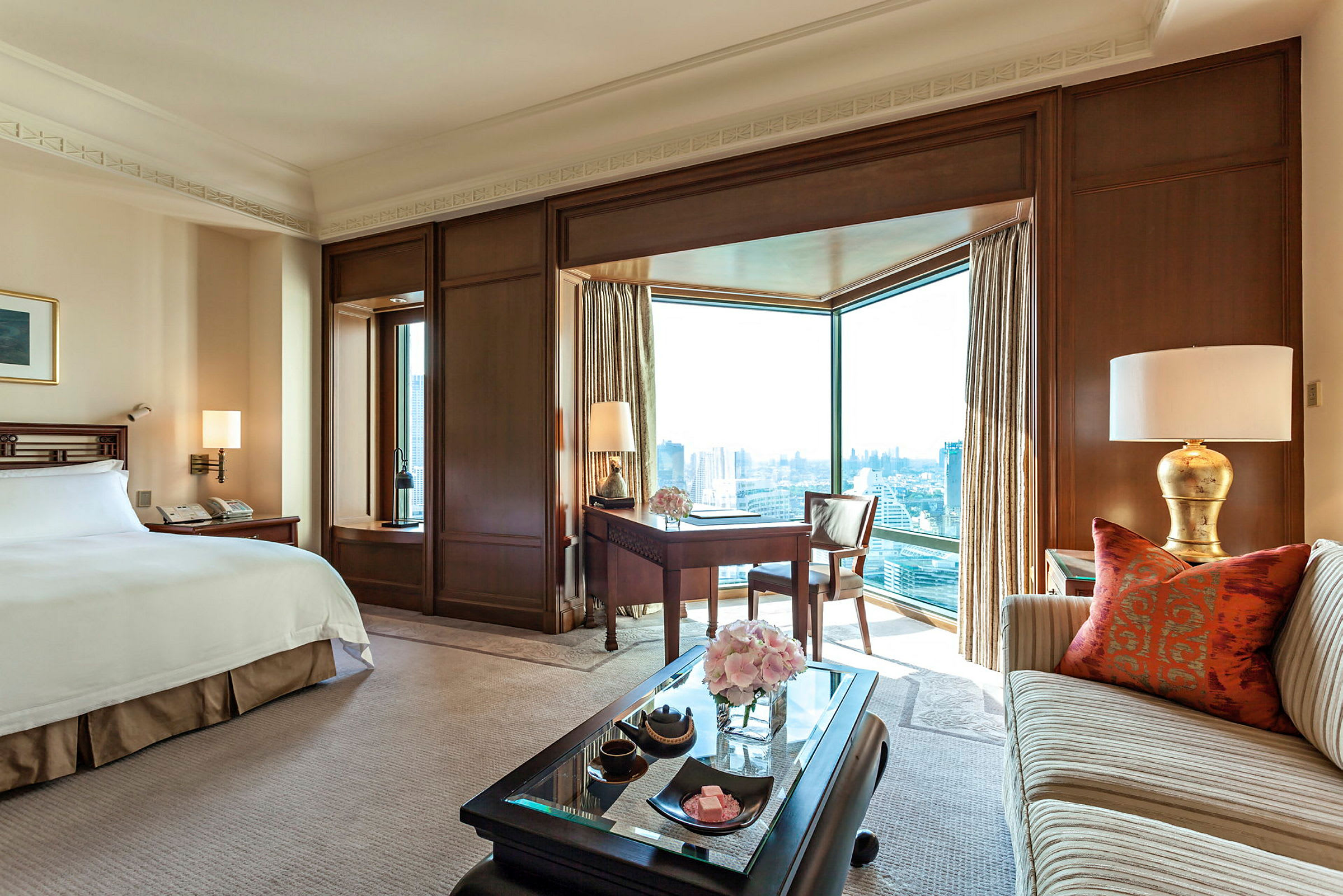 Ett elegant hotellrum med en stor säng, en soffa, ett skrivbord och stora fönster med utsikt över staden. (AI-genererad text)