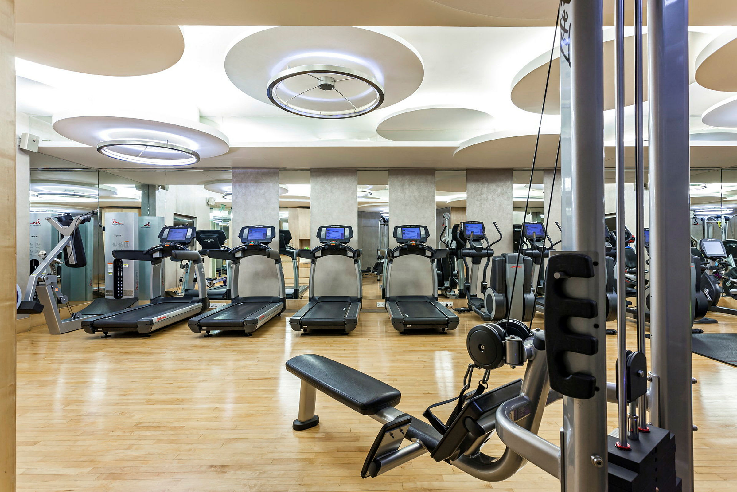 Ett gym med träningsutrustning såsom löpband och styrketräningsmaskiner. Trägolv och modern belysning. (AI-genererad text)