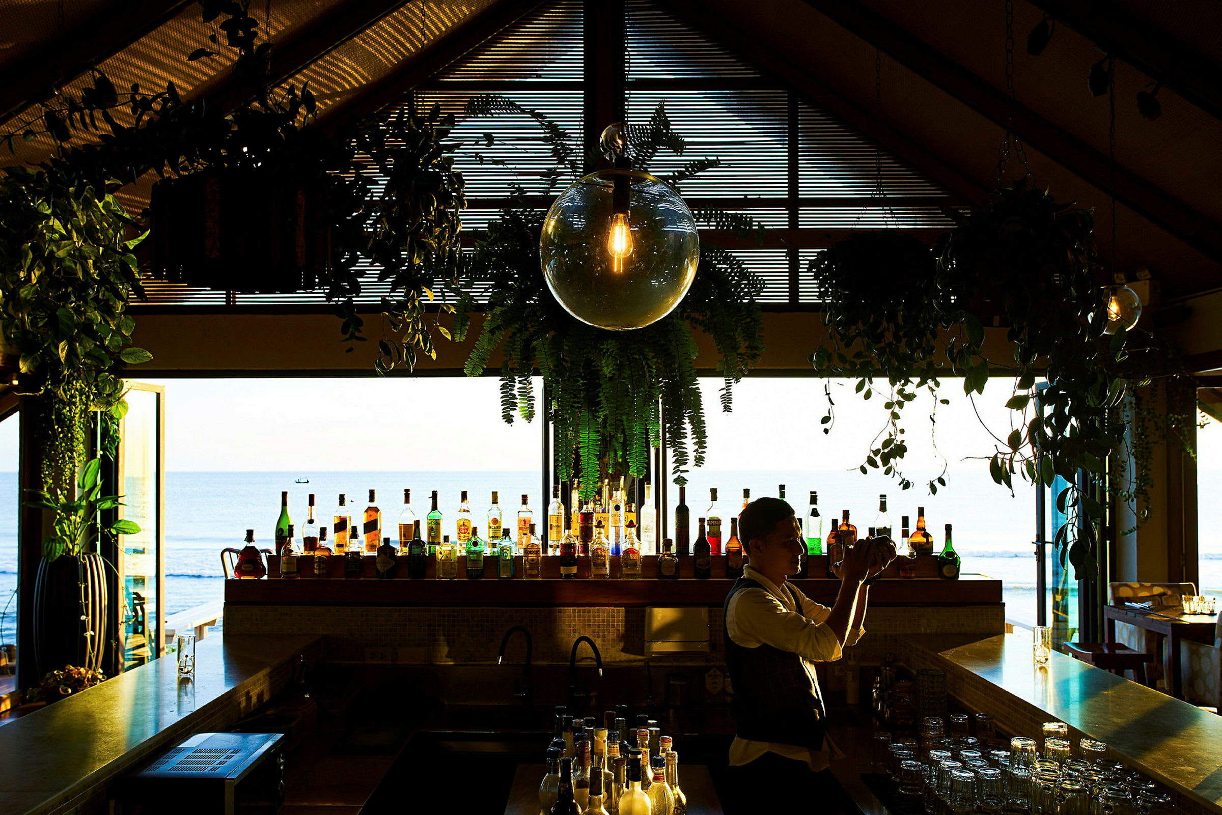 En bar med olika flaskor och dekorationer i ett rum med utsikt ut mot havet. (AI-genererad text)