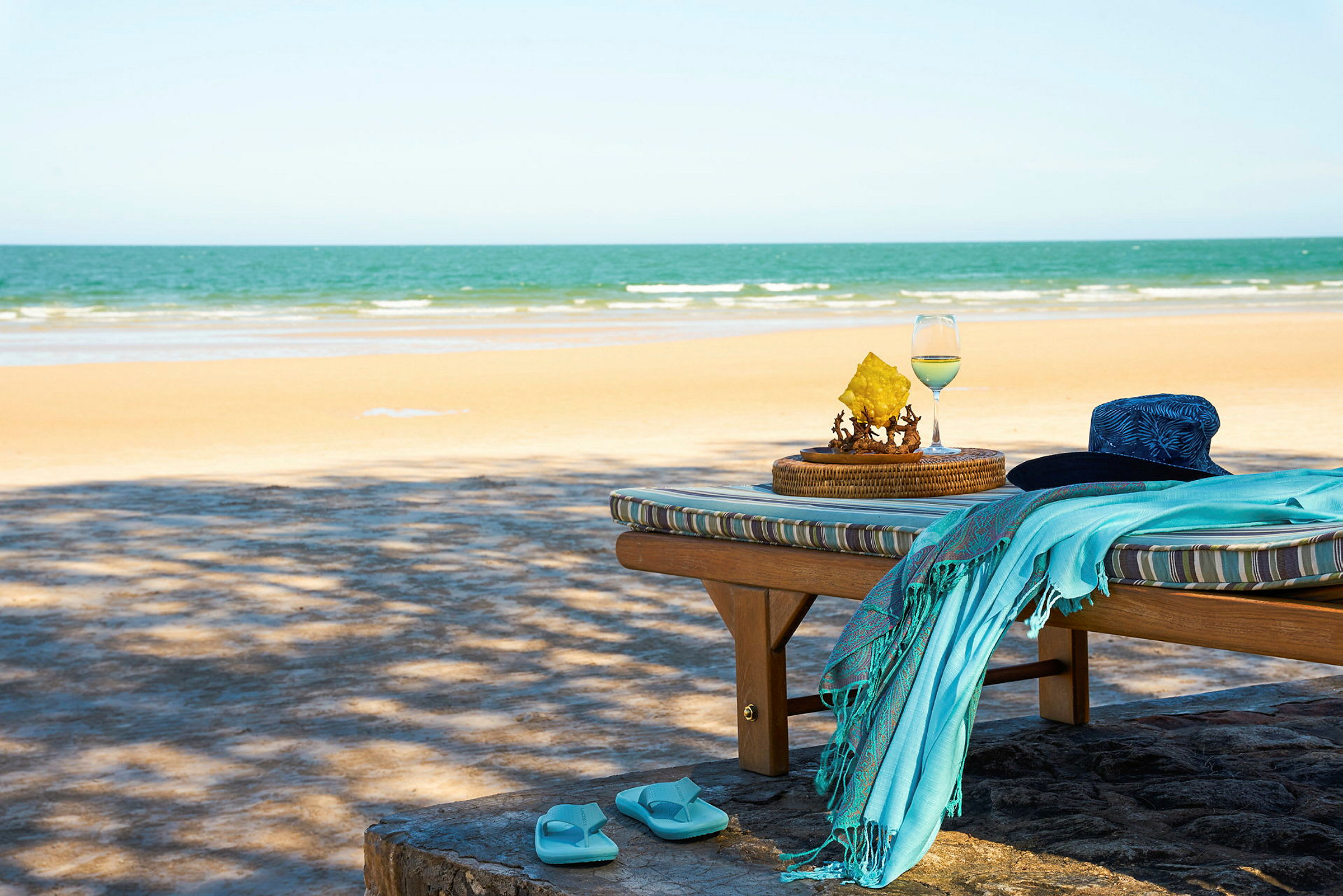 Solstol med en hatt, handduk och flip-flop-sandaler vid stranden. (AI-genererad text)