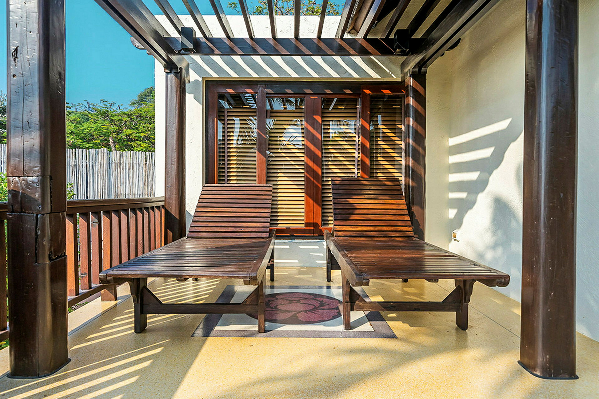 Två träliggstolar står på en solig veranda under en pergola. (AI-genererad text)