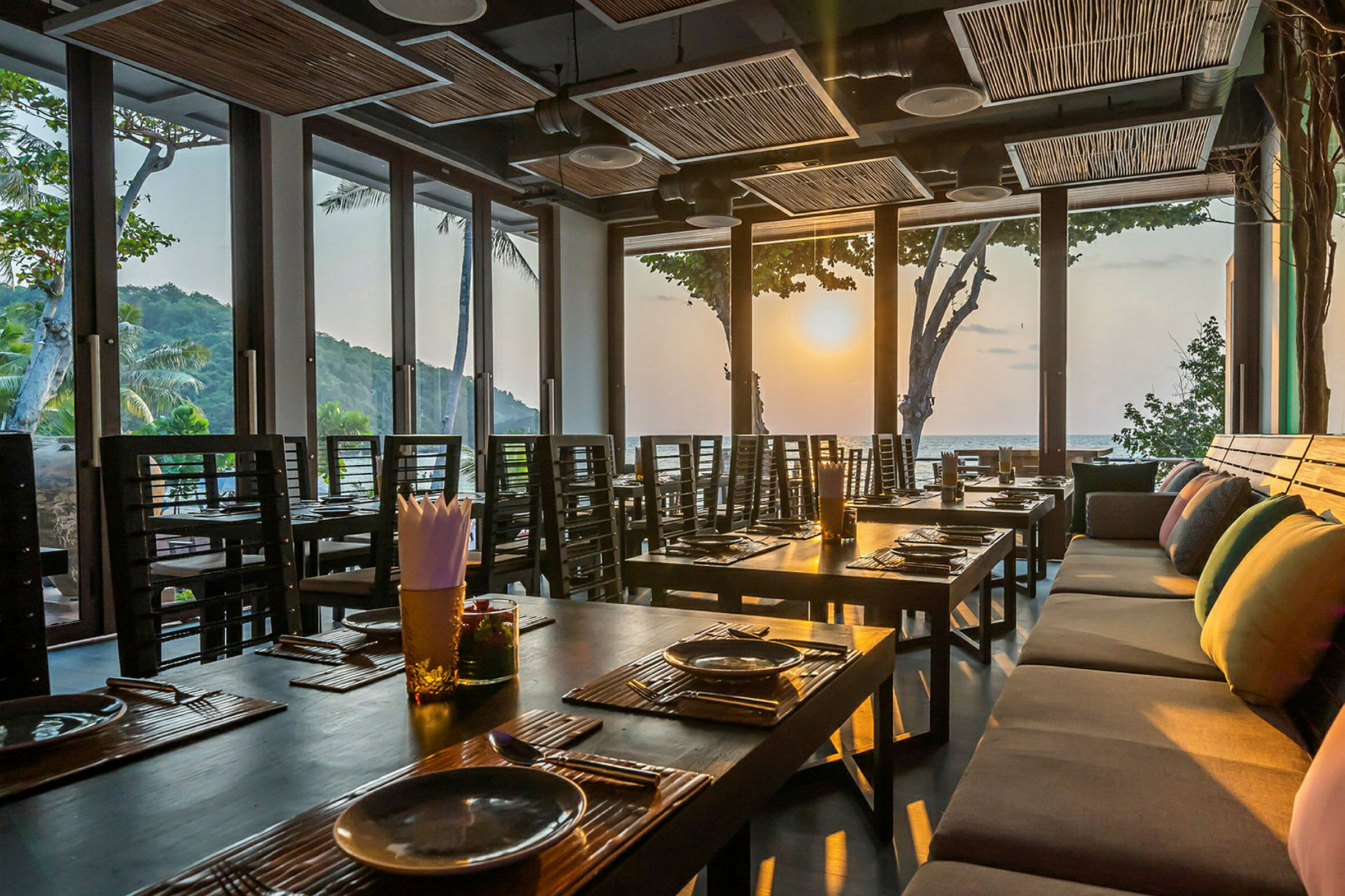 Interiör av en restaurang med dukade bord och stora fönster som släpper in ljus från solnedgången. (AI-genererad text)
