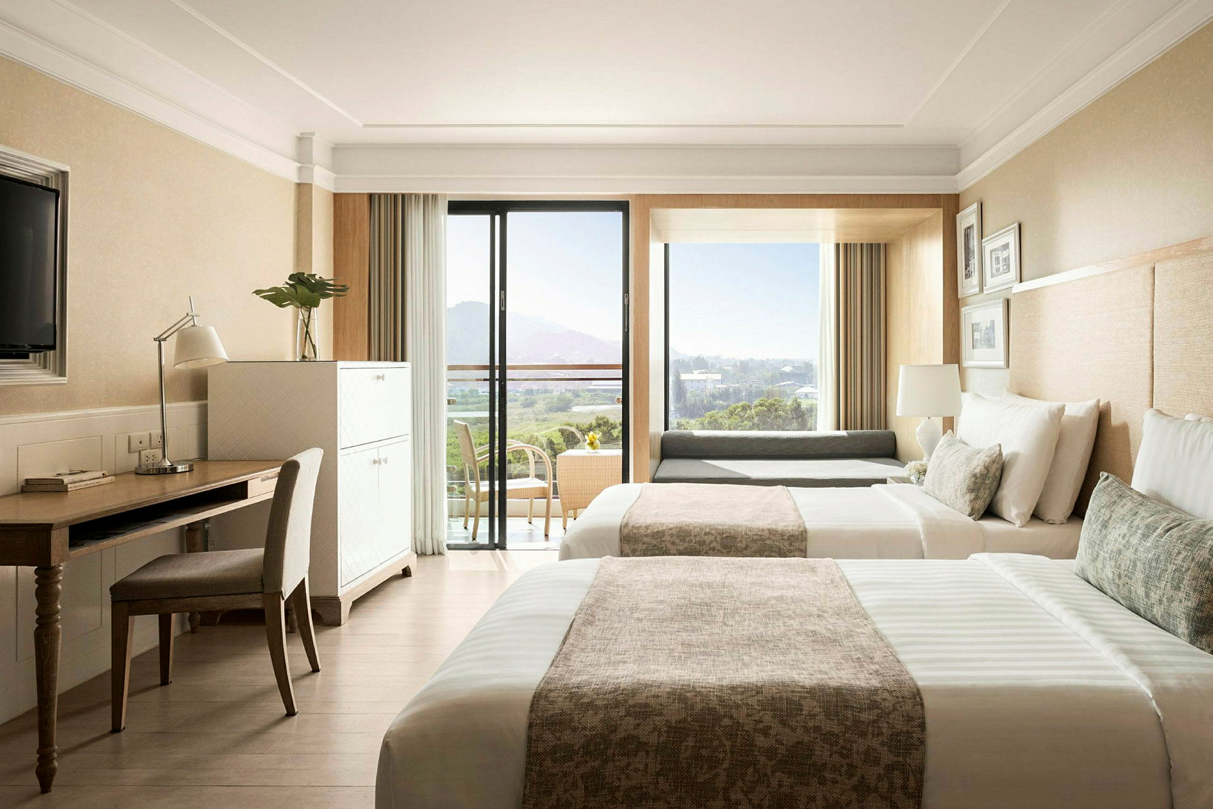 Ett hotellrum med två sängar, ett skrivbord, en stol och en balkong med utsikt över landskapet. (AI-genererad text)