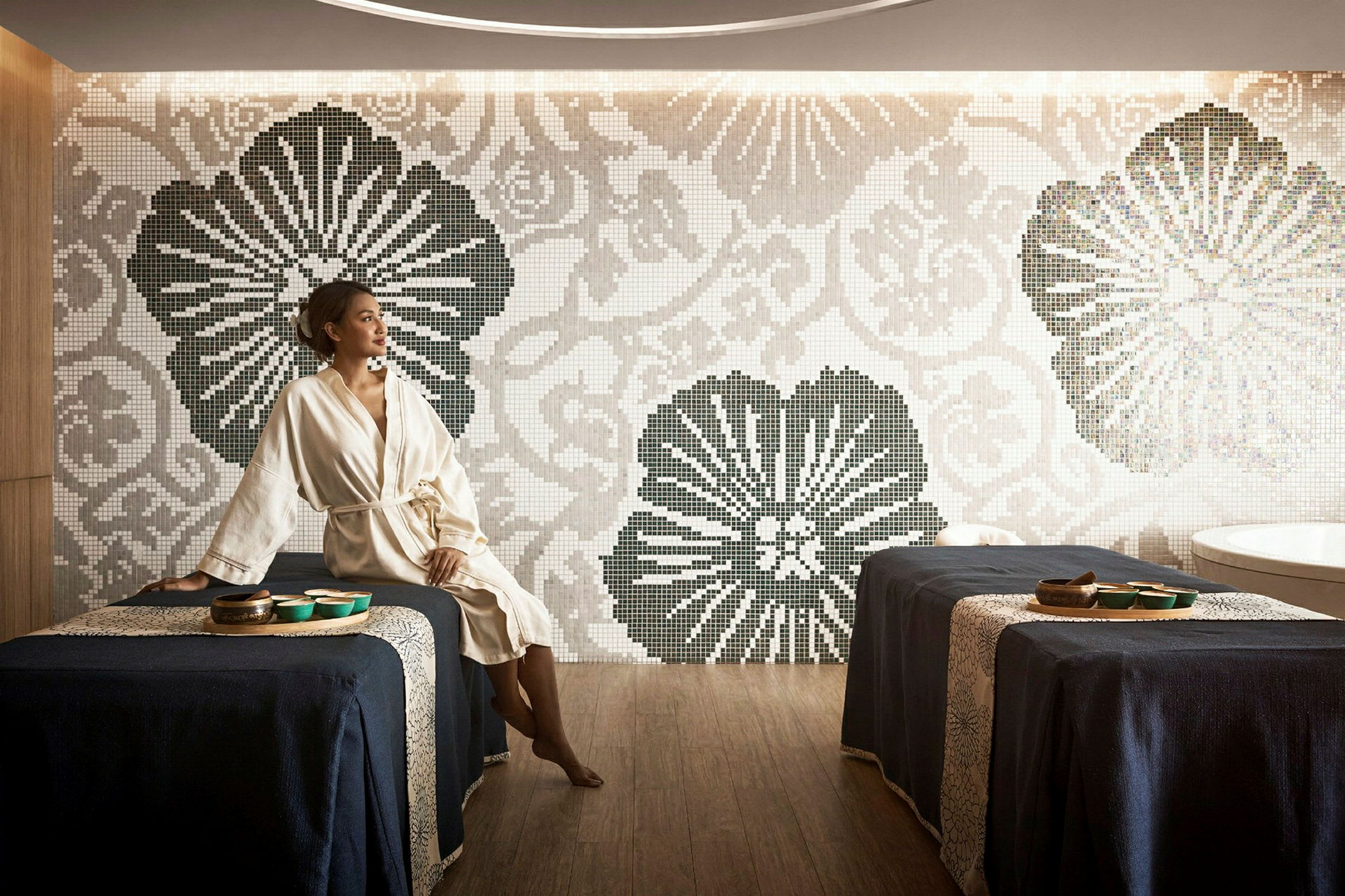 Ett spa med två massagebäddar klädda i mörkblå tyg, mosaikvägg med blommigt mönster och ett badkar i bakgrunden. (AI-genererad text)