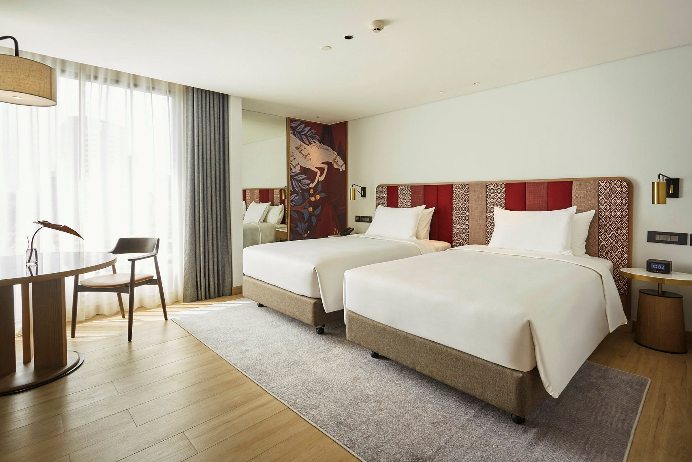 Ett hotellrum med två enkelsängar, ett runt bord med en stol och ett stort fönster med gardiner. (AI-genererad text)