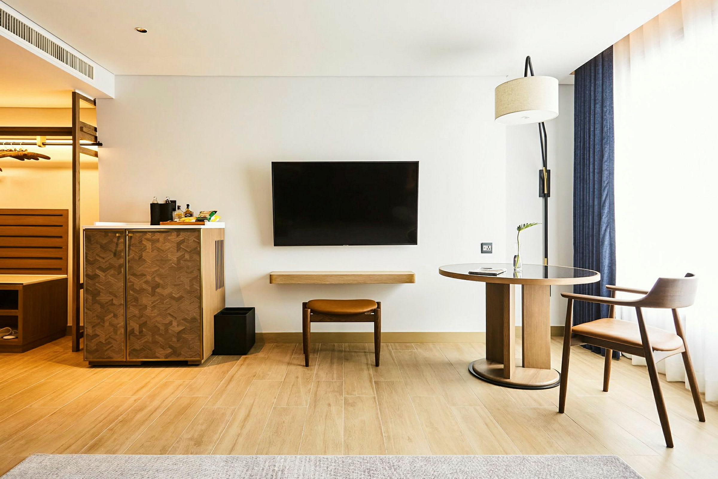 Ett hotellrum med trämöbler, en tv på väggen och ett stort fönster med gardiner. (AI-genererad text)