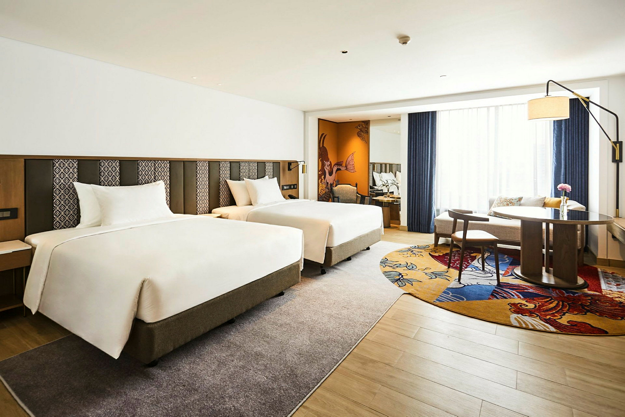 Hotelrum med två separata sängar, ett bord och stolar samt soffhörna. (AI-genererad text)