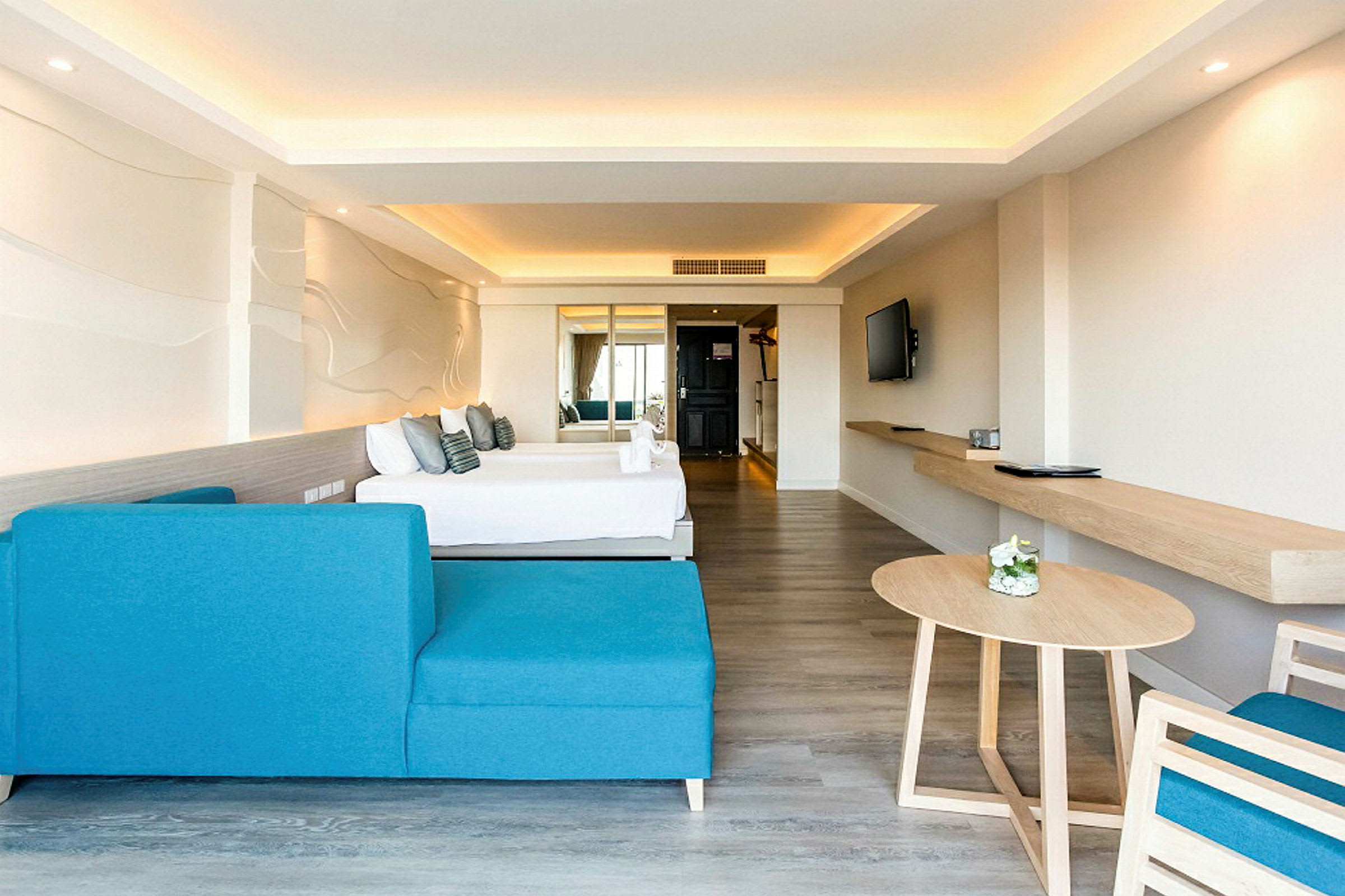 Ett modernt hotellrum med en blå soffa, ett bord och en säng i bakgrunden. Väggen har en dekorativ design, och rummet är ljust med neutrala färger. (AI-genererad text)