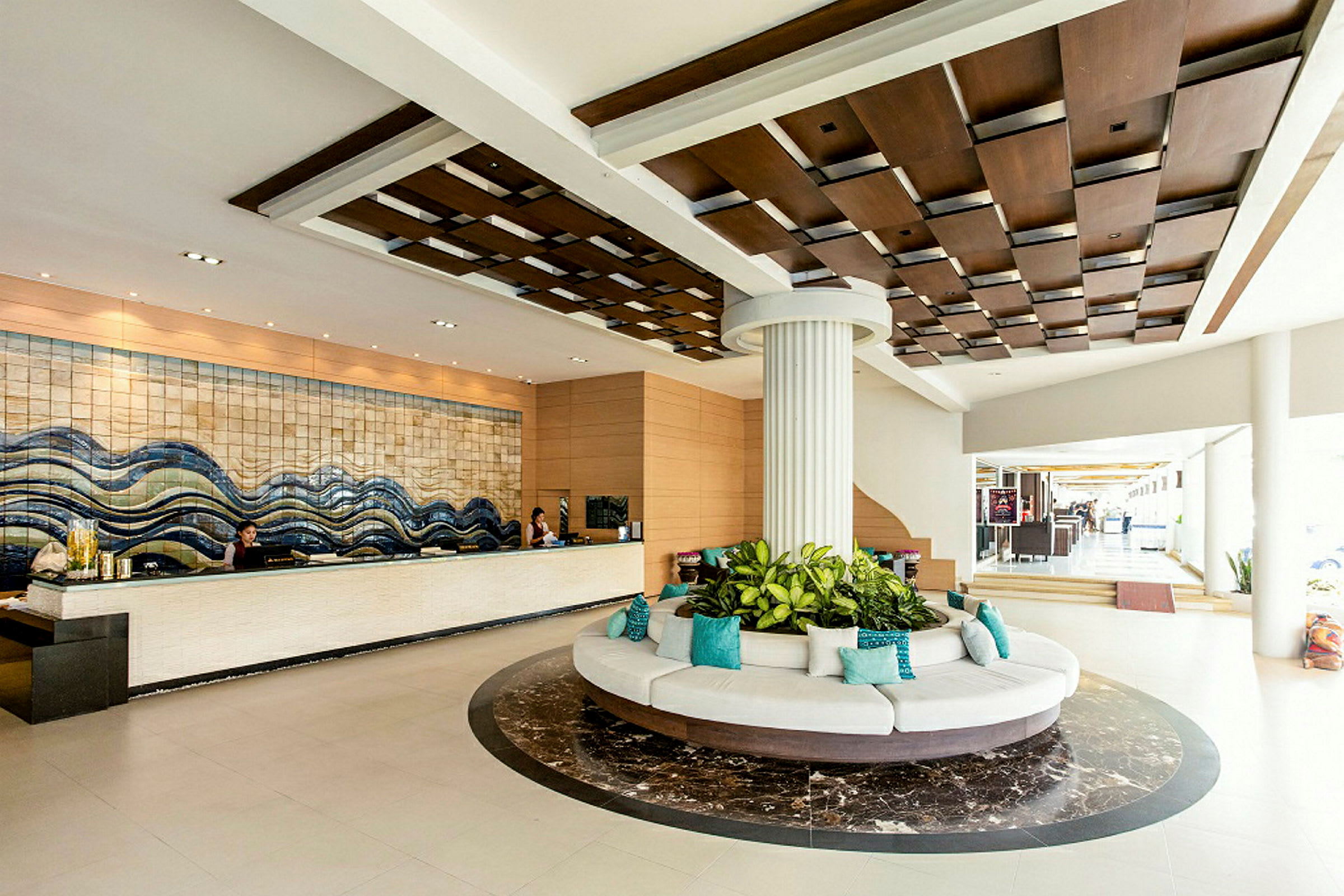 Hotellets lobby med en reception, en rund sittgrupp med växter i mitten och en dekorativ takdesign. (AI-genererad text)