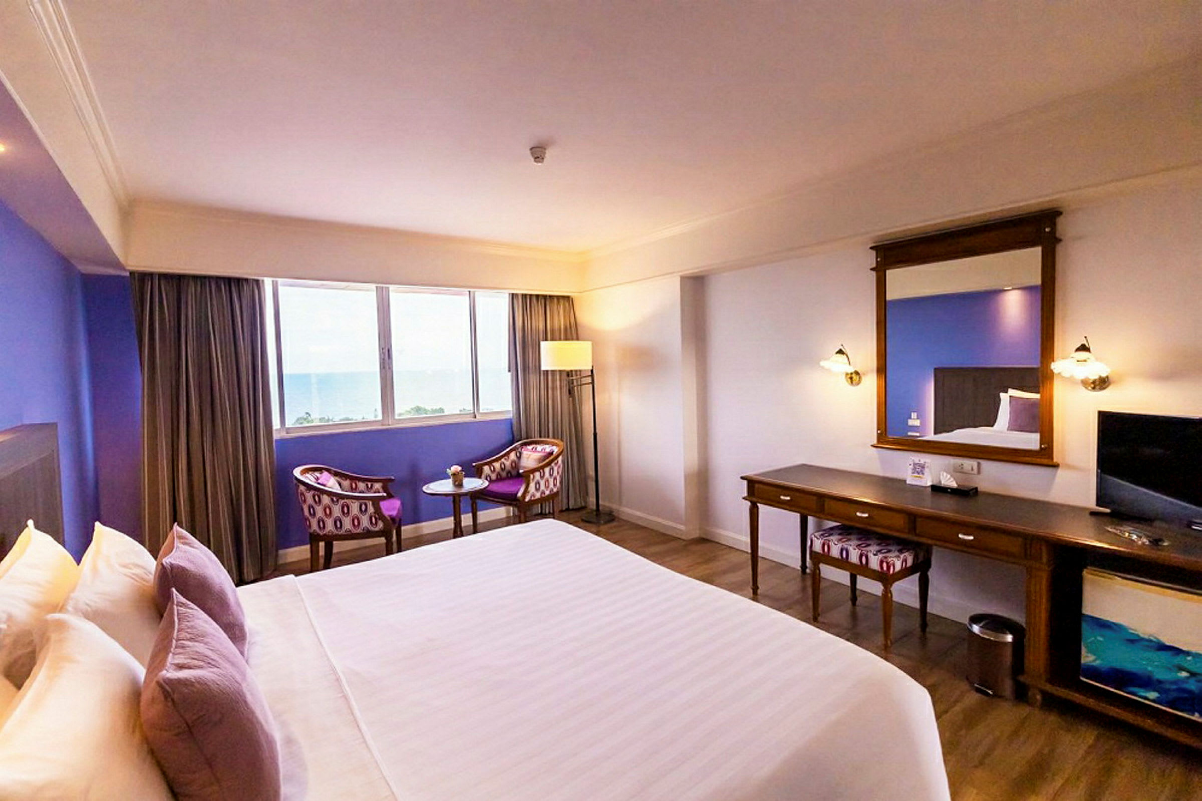 Ett hotellrum med en stor säng, sittgrupp vid ett fönster och ett skrivbord med spegel. (AI-genererad text)