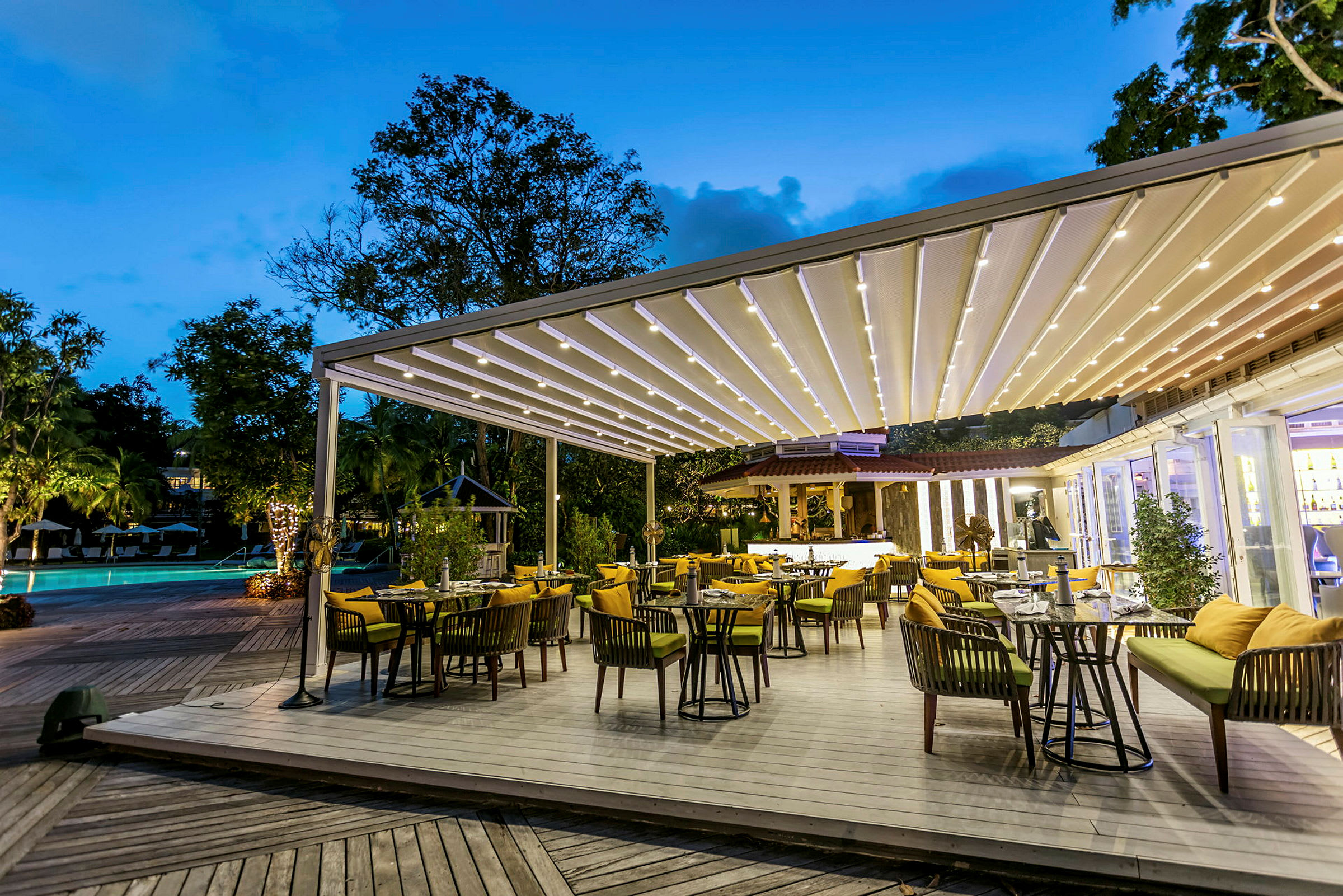Restaurang med utomhusterrass och takbelysning bredvid en pool på kvällen. (AI-genererad text)