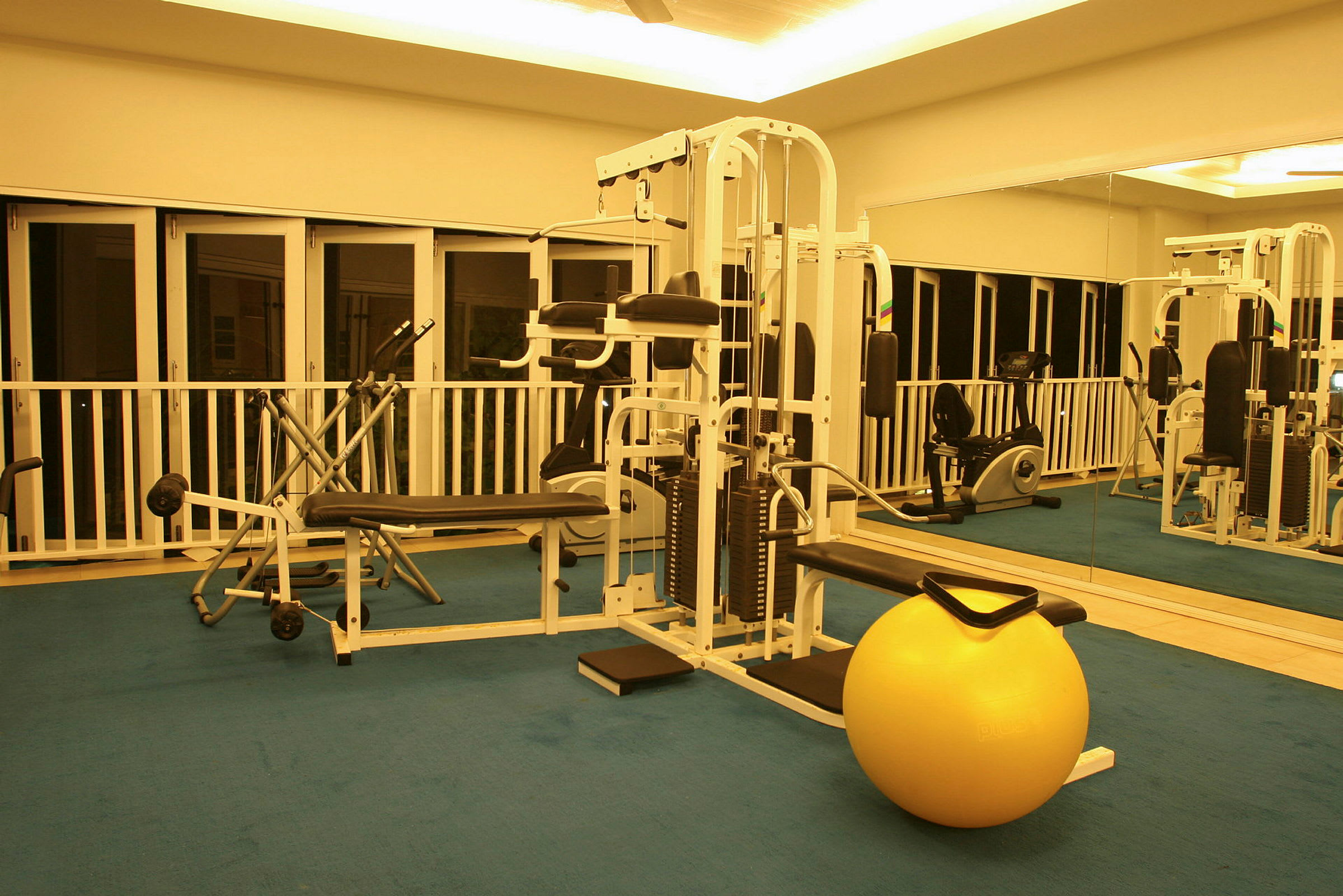 Interiör av ett gym med träningsutrustning och en gul balansboll på golvet. (AI-genererad text)