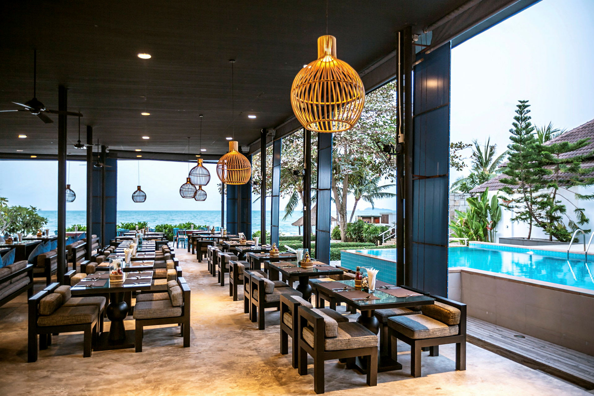 En restaurang med sittplatser utomhus vid en pool, med havet i bakgrunden. (AI-genererad text)