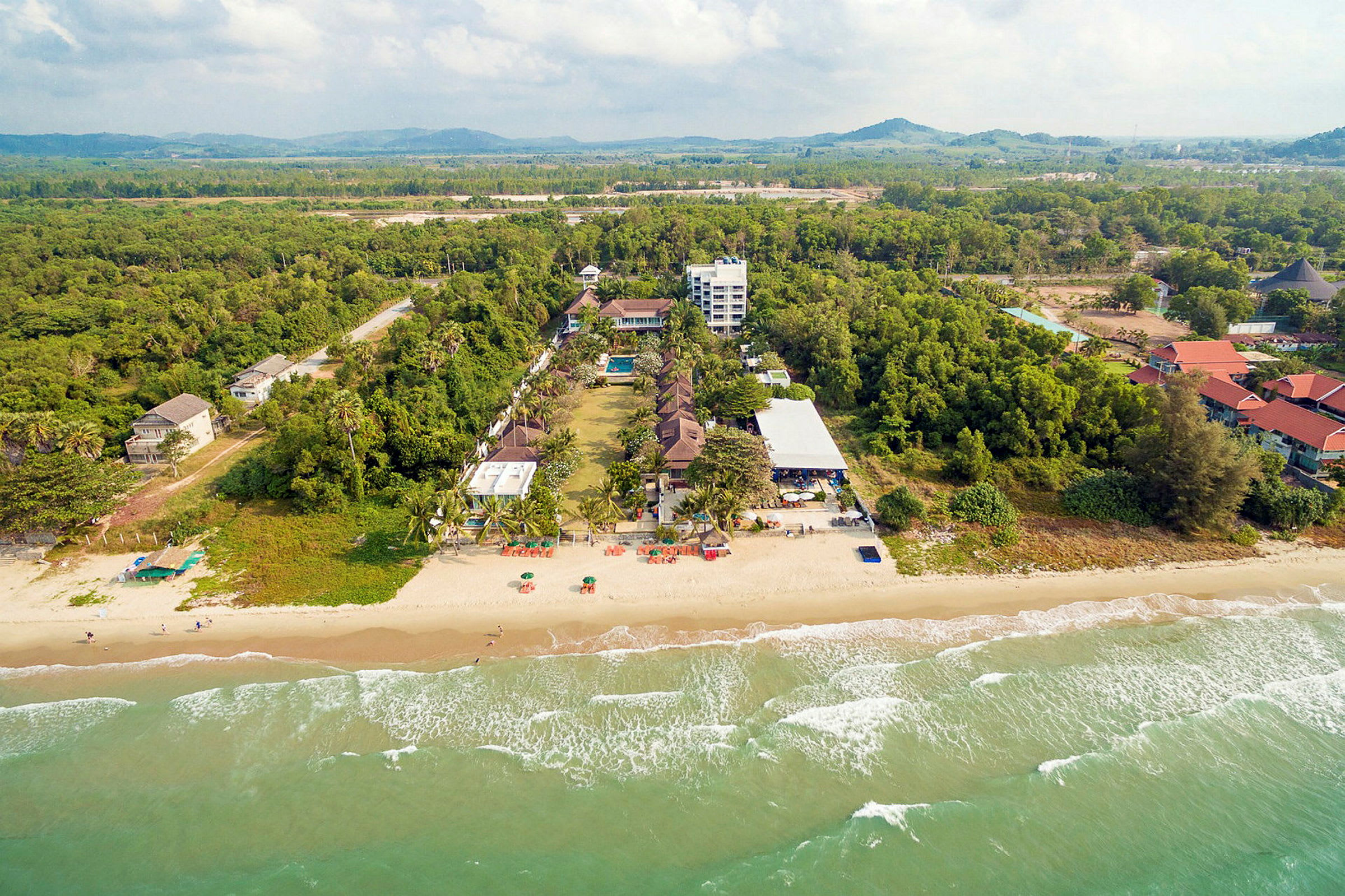 Flygfoto av en strand och ett hotellområde omgivet av grönska. (AI-genererad text)