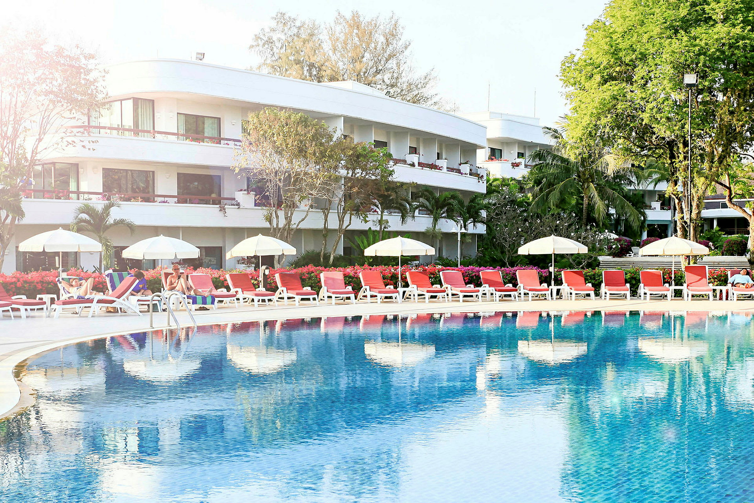 Poolområde med solstolar och parasoller framför ett hotell. (AI-genererad text)